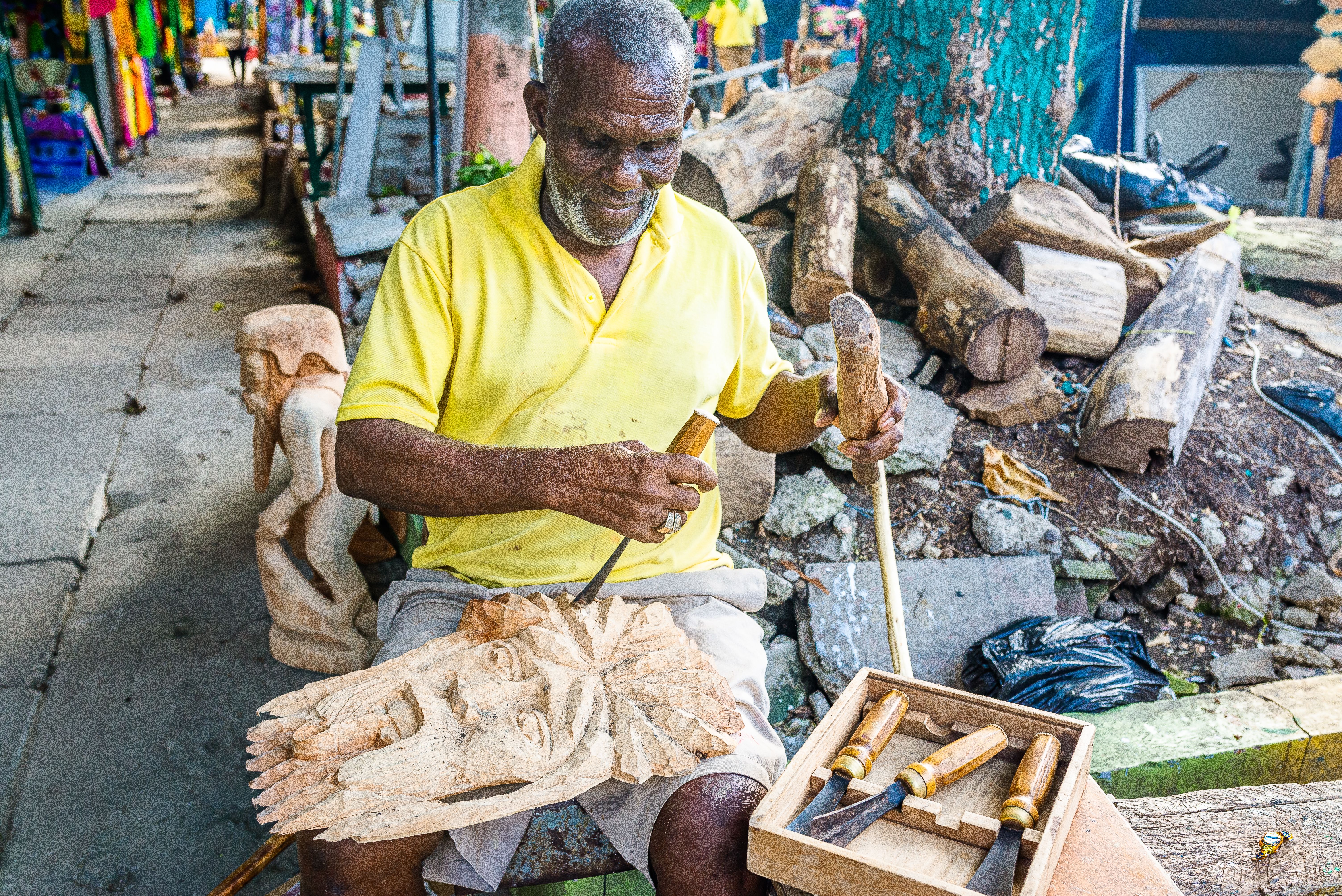 Jamaican man uses hand tools to carve a decorative art sculpture from raw wood Jamaican man uses hand tools to carve a decorative art sculpture from raw wood