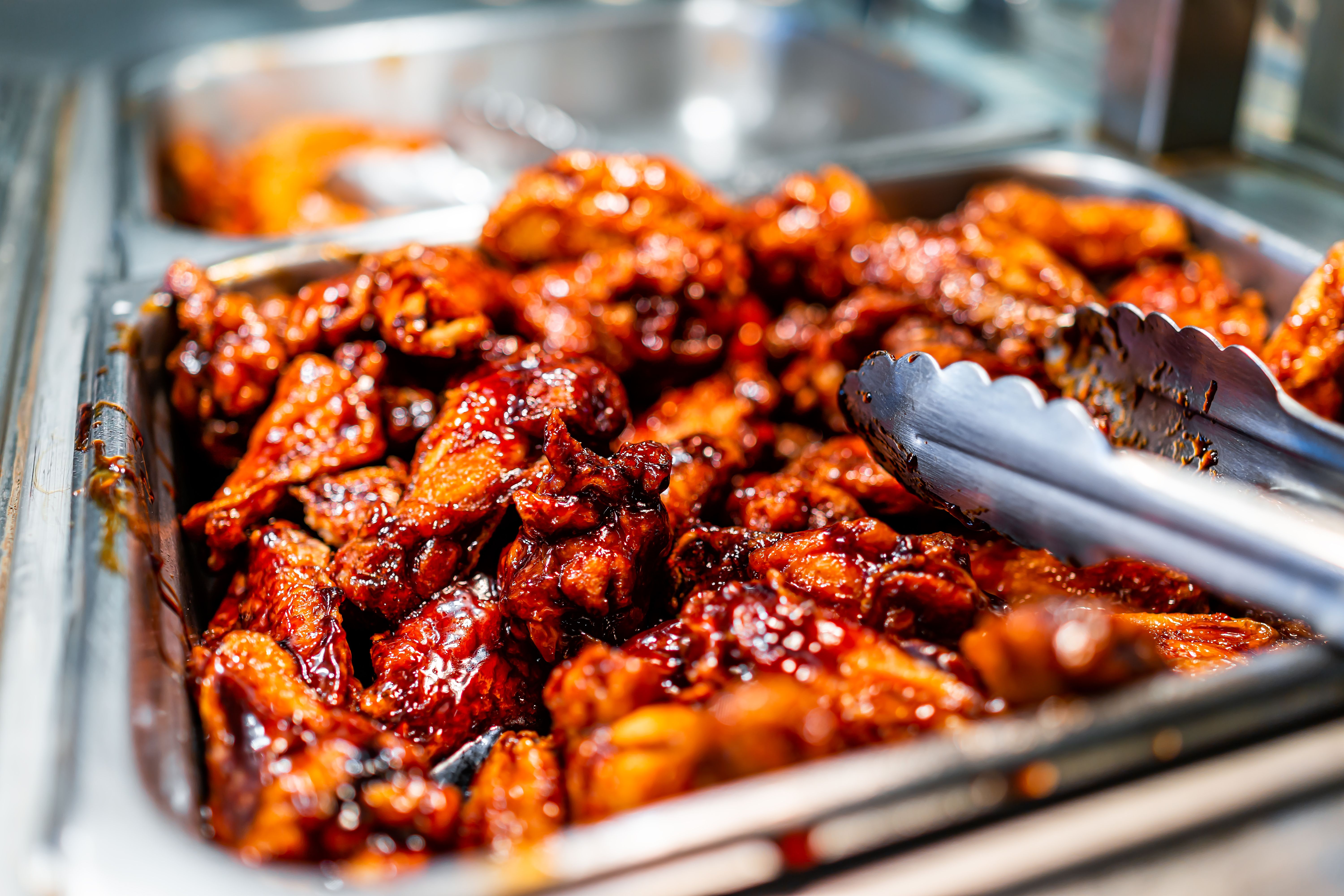 Barbeque sauce chicken wings buffet bar self serve with tongs in grocery store, restaurant or catering event with red color unhealthy food Barbeque sauce chicken wings buffet bar self serve with tongs in grocery store, restaurant or catering event with red color unhealthy food