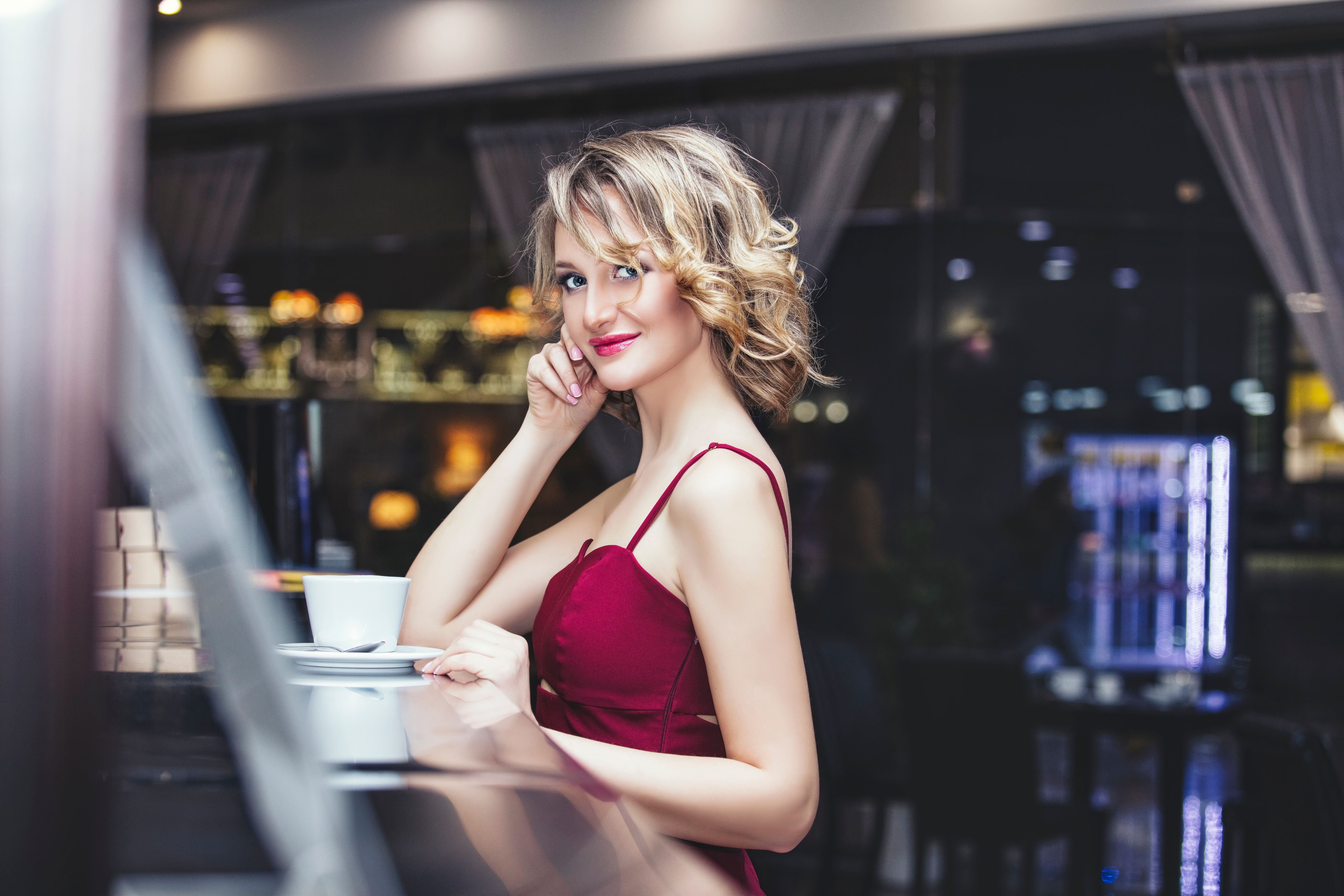 Beautiful woman blonde model in a red jumpsuit elegant with a Cup of coffee in the restaurant Beautiful woman blonde model in a red jumpsuit elegant with a Cup of coffee in the restaurant