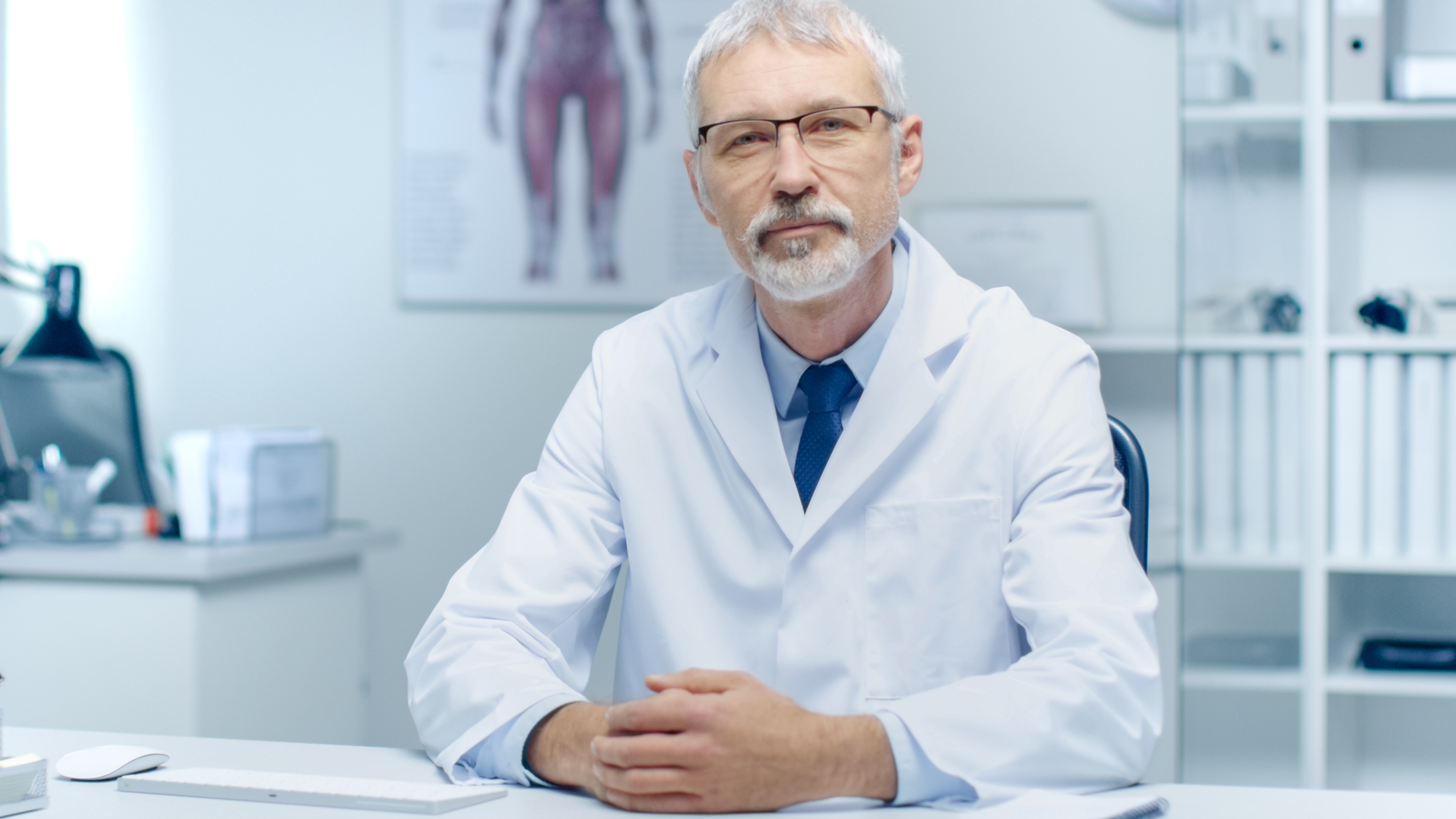 Experienced Gray Haired Senior Medical Practitioner Smiling and Looking Into Camera. Portrait Shot in Modern and Light Office.
