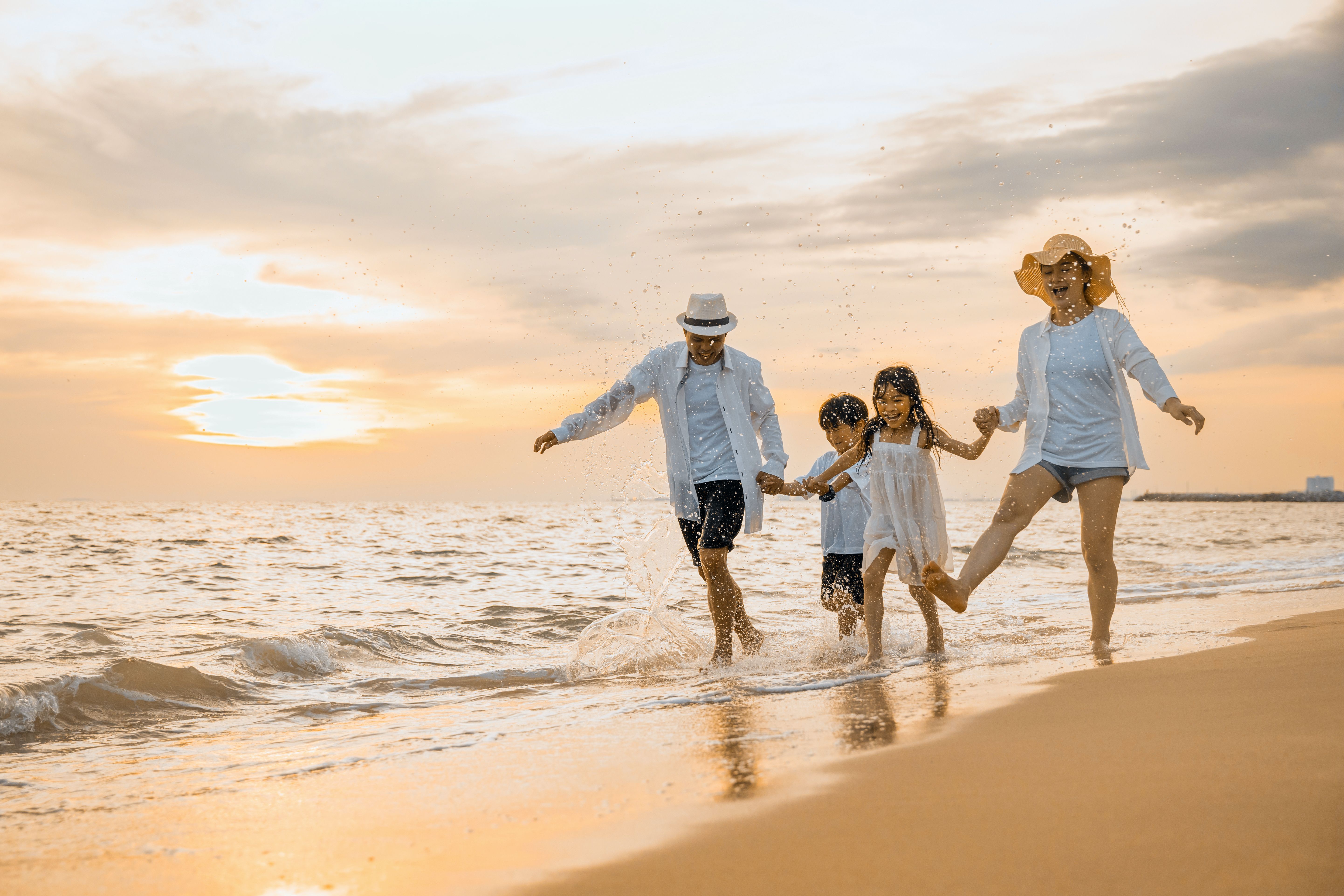 Happy family having fun running on a sandy beach at sunset time