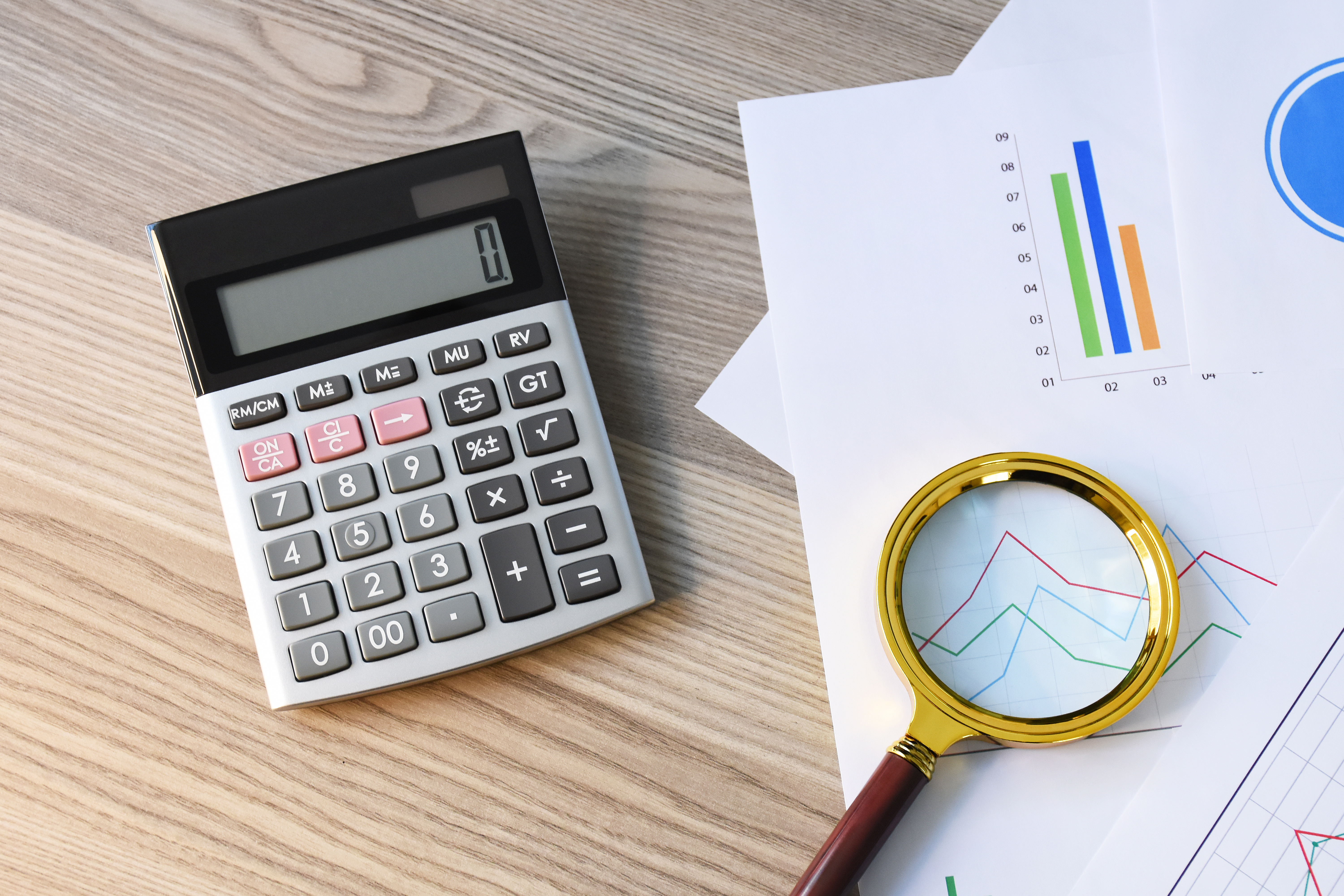 Calculator, financial charts, and magnifying glass symbolizing detailed analysis and investigation in fraud prevention and detection.