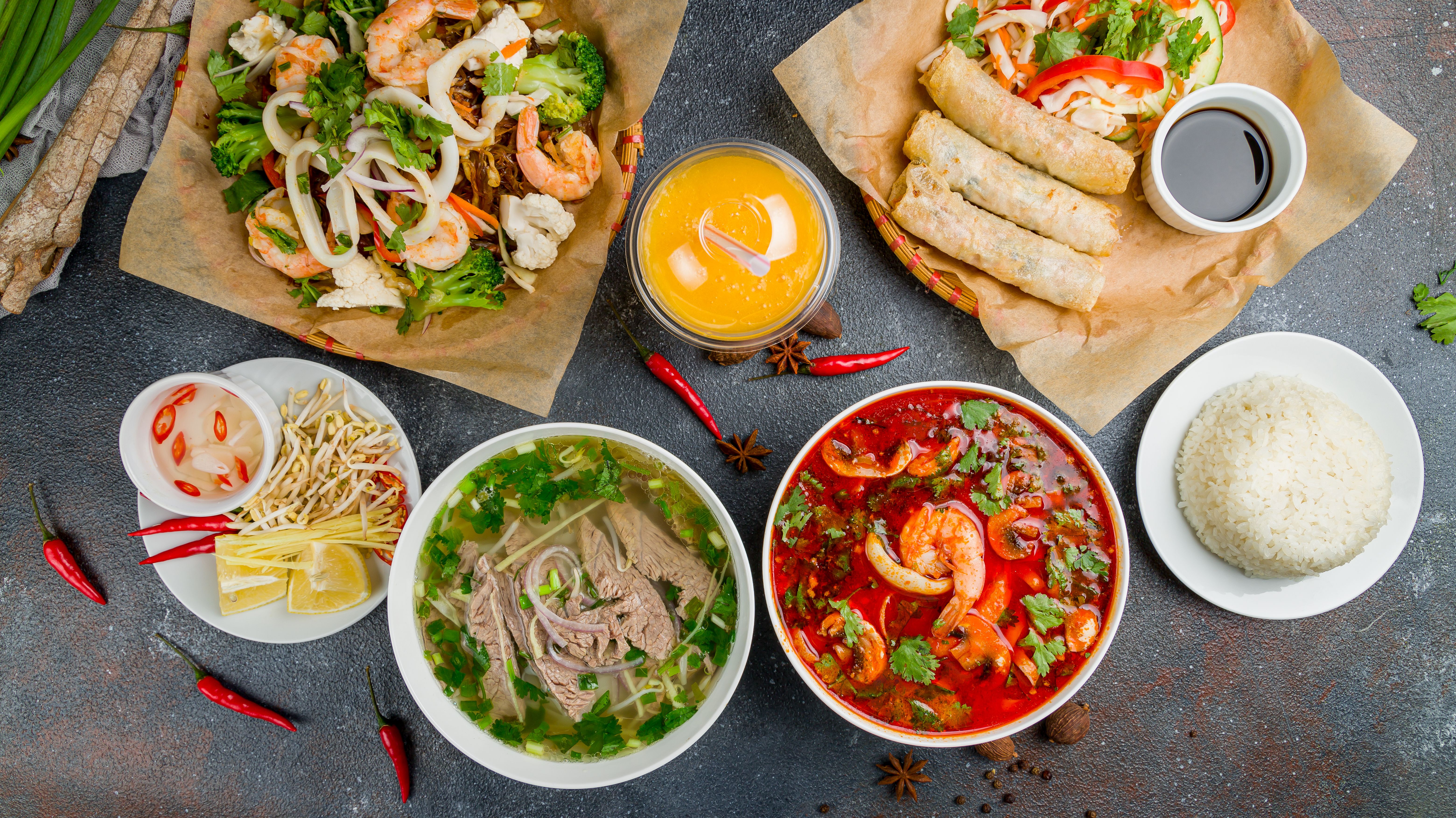 Assorted asian dinner, vietnamese food. Pho bo, pho tom, noodles, spring rolls, tom yam, rice, mango shake on beautiful black stone table top view