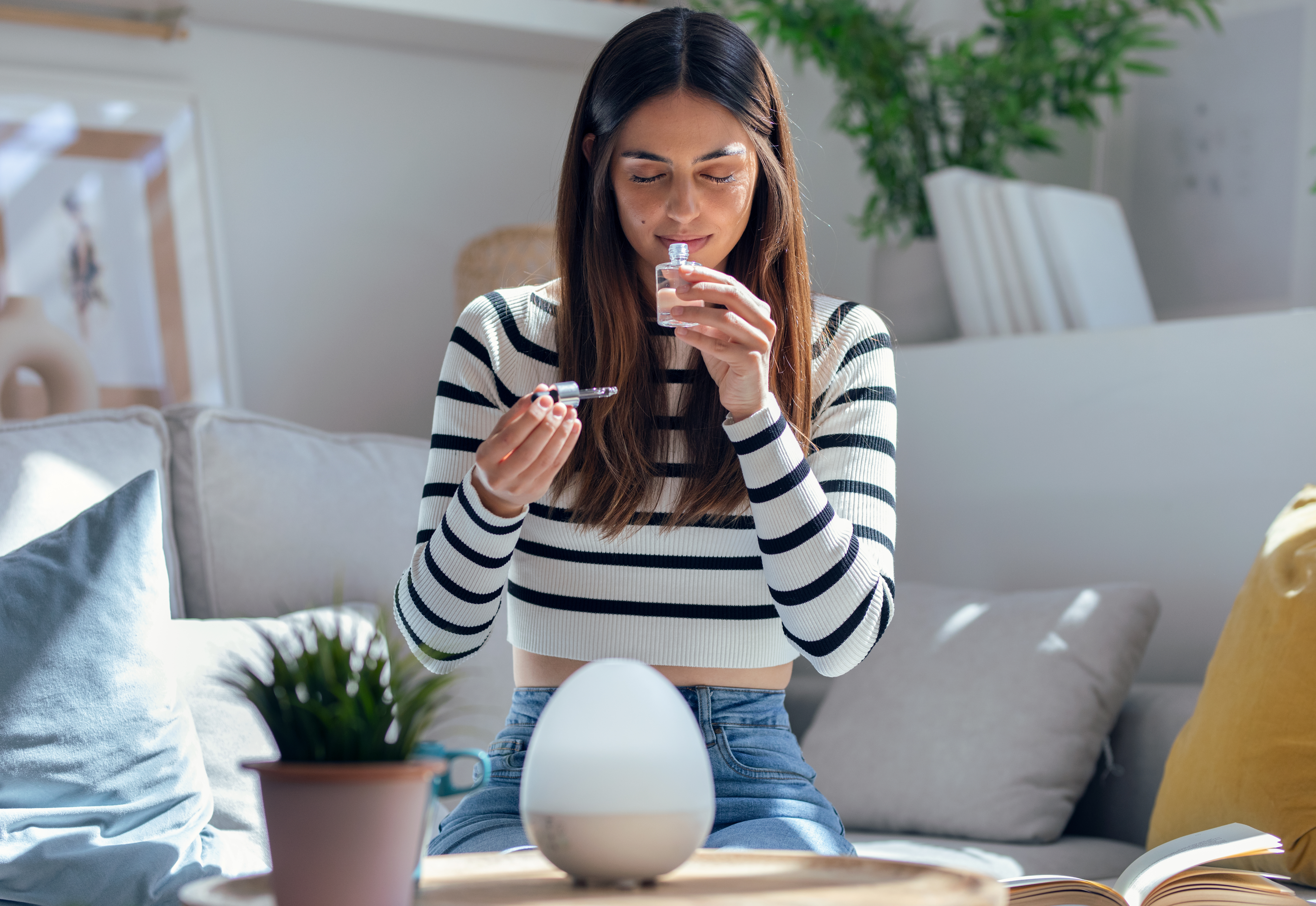 Cheerful woman girl holding a bottle of essential oil while testing it sitting on a couch at home.