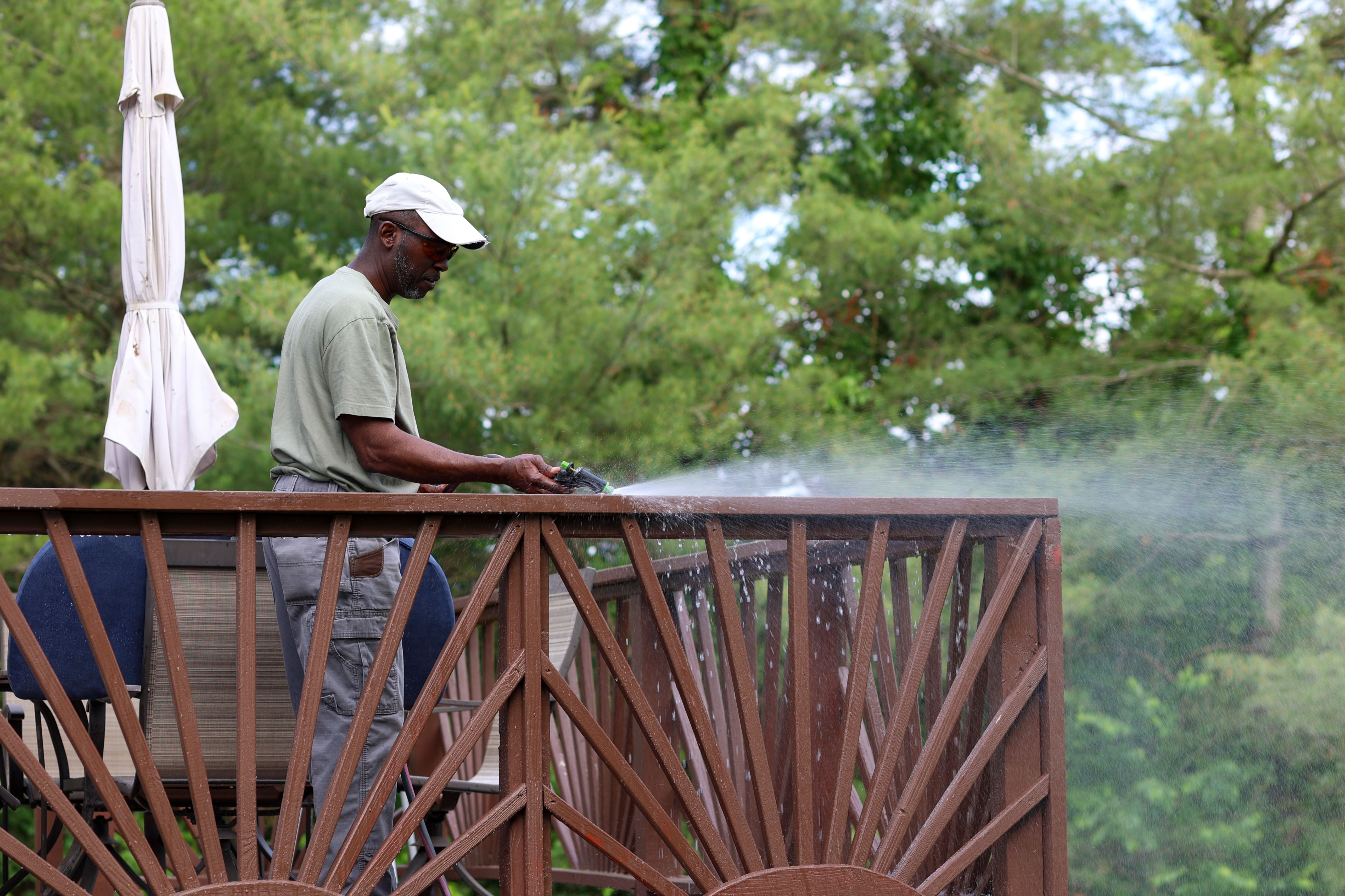 A Portrait Of A Black Man Power Washing A Wooden Deck