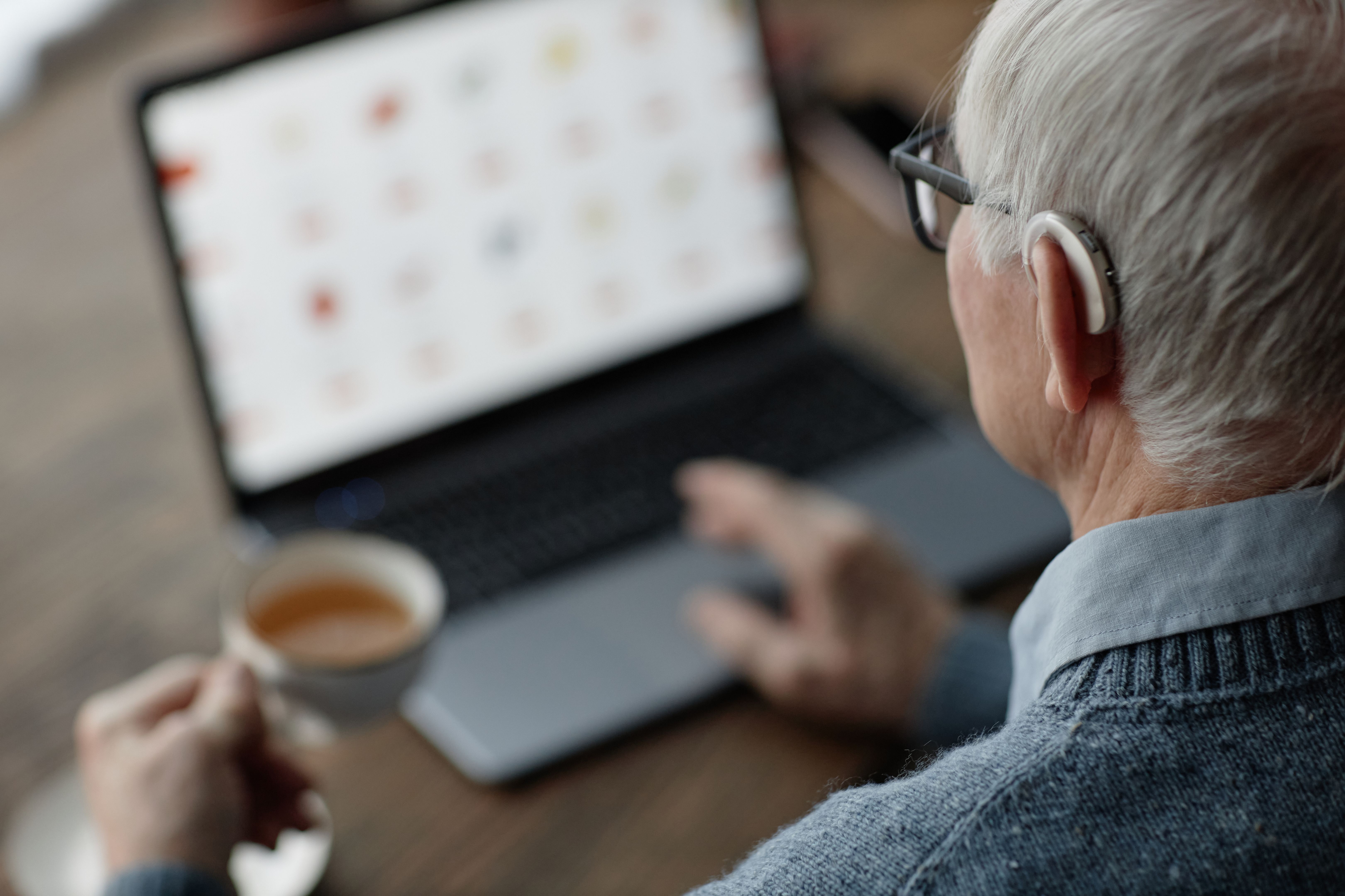 Elderly Cagary Man Wearing Hearing Aid Working on Laptop at Home while Using Assistive Technology