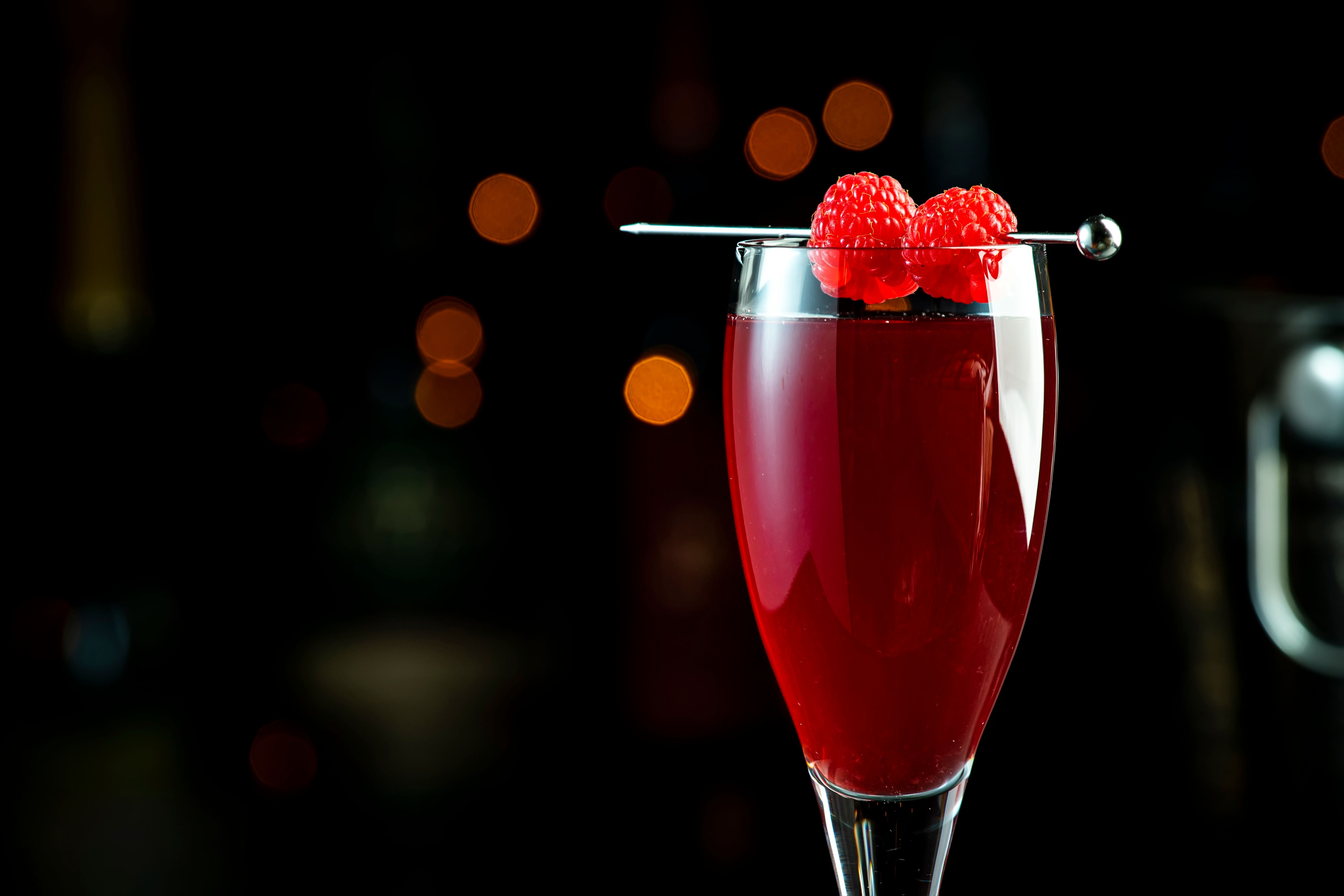 Delicious alcoholic cocktail with raspberries, lychees and French sparkling wine, black background with bottles