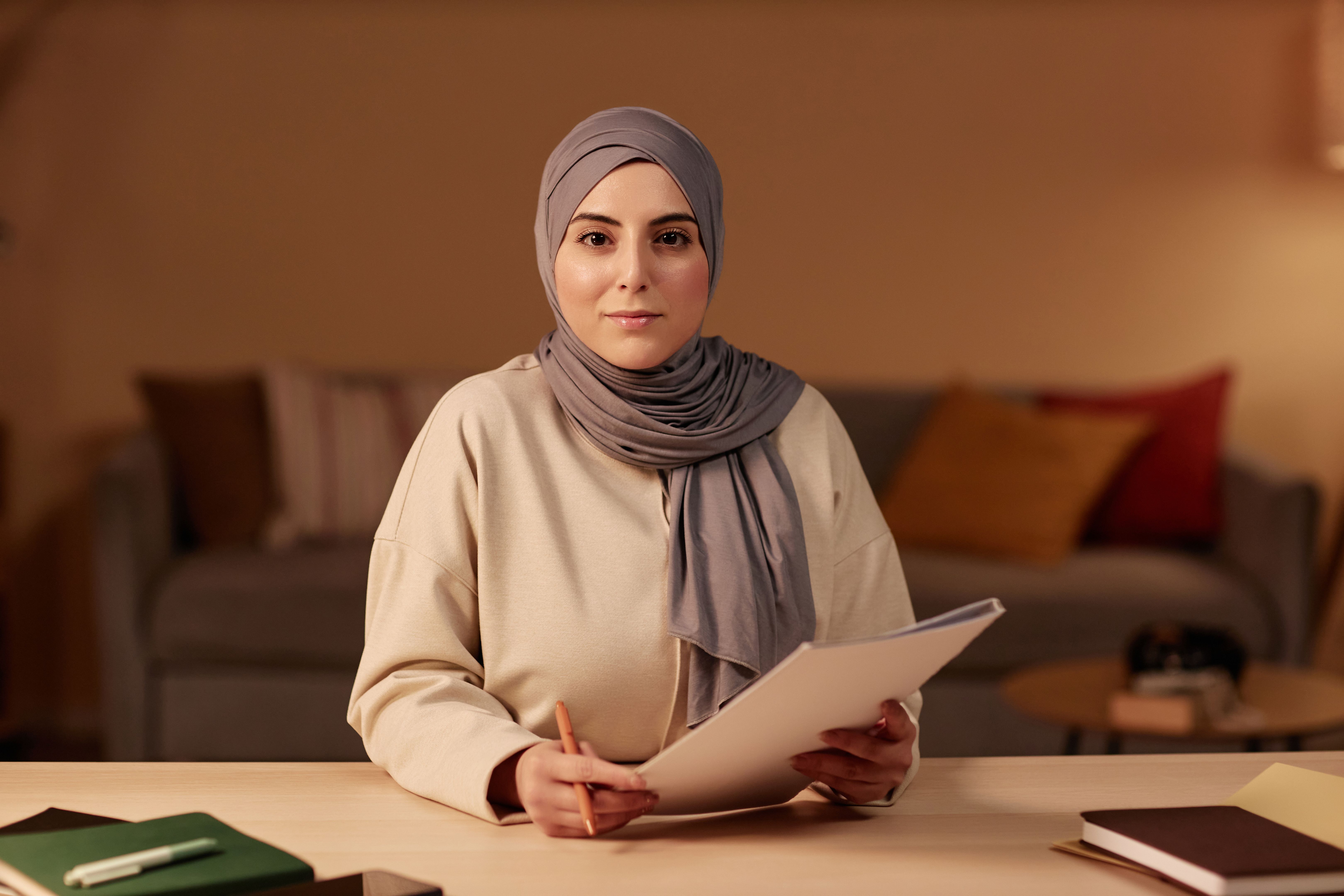 Young confident businesswoman in hijab and casualwear sitting by desk