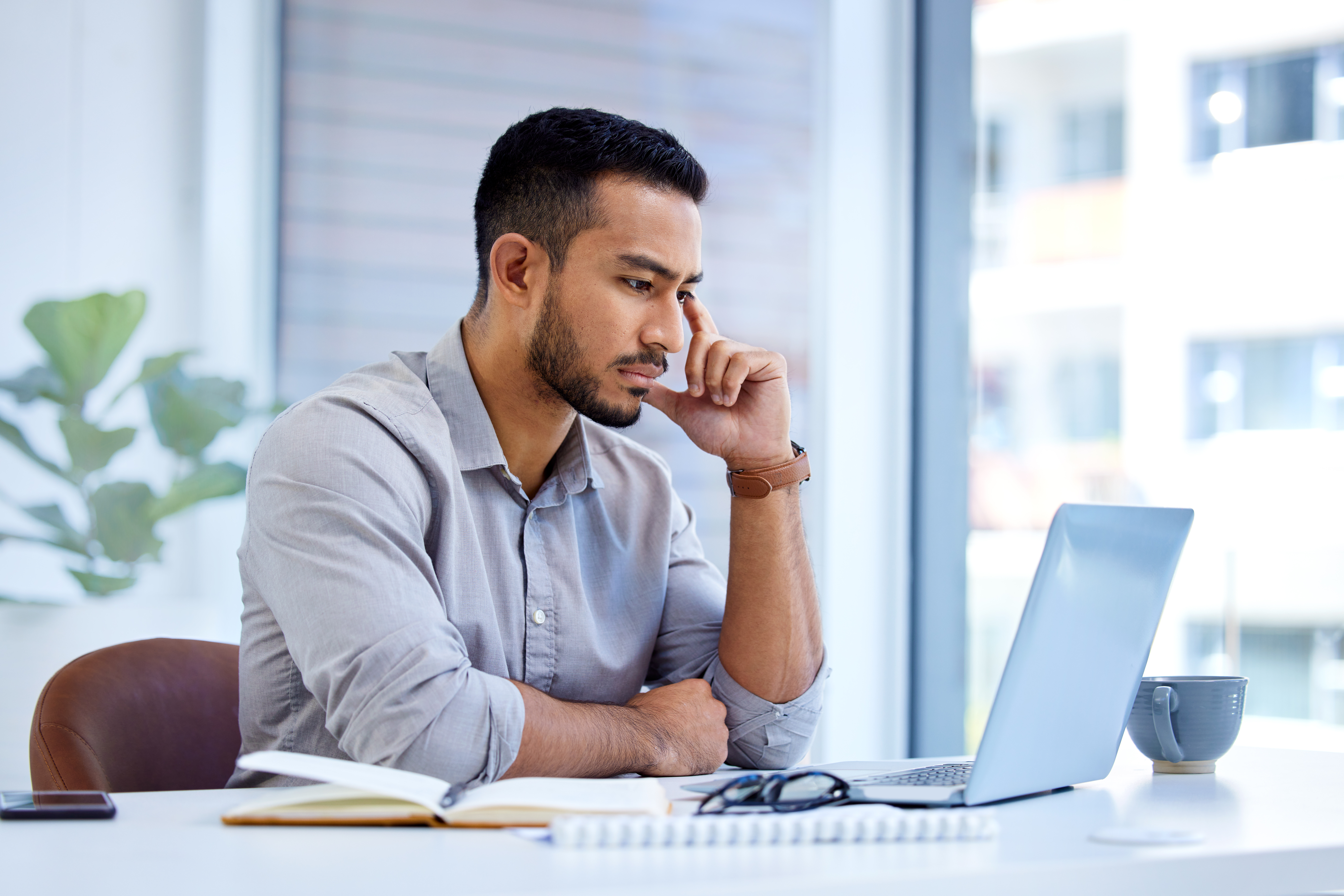 Shot of a young businessman working on a laptop in an office Shot of a young businessman working on a laptop in an office