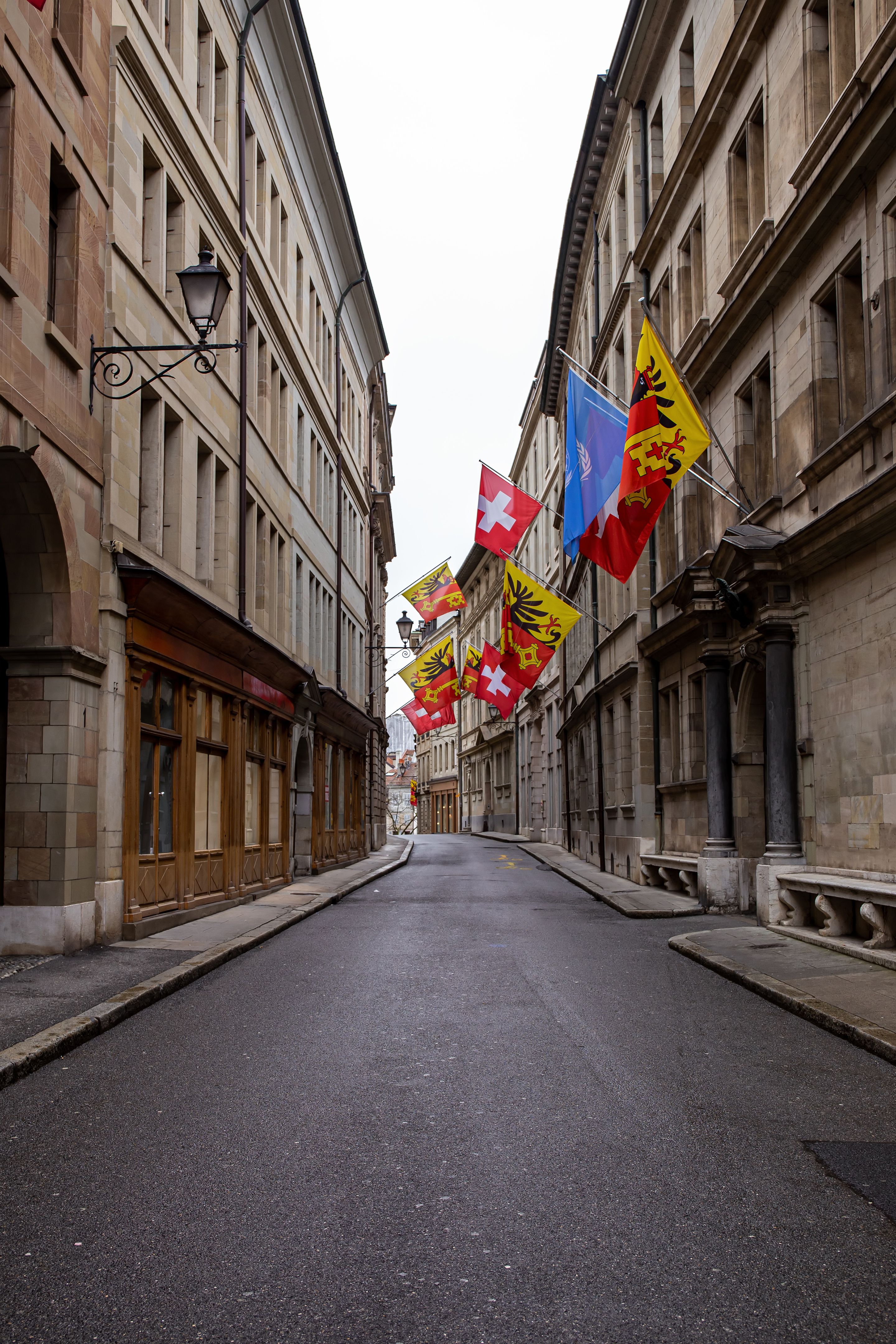 Street in Geneva, Switzerland has buildings and is lined with various flags, including Swiss flag, featuring white cross on red background
