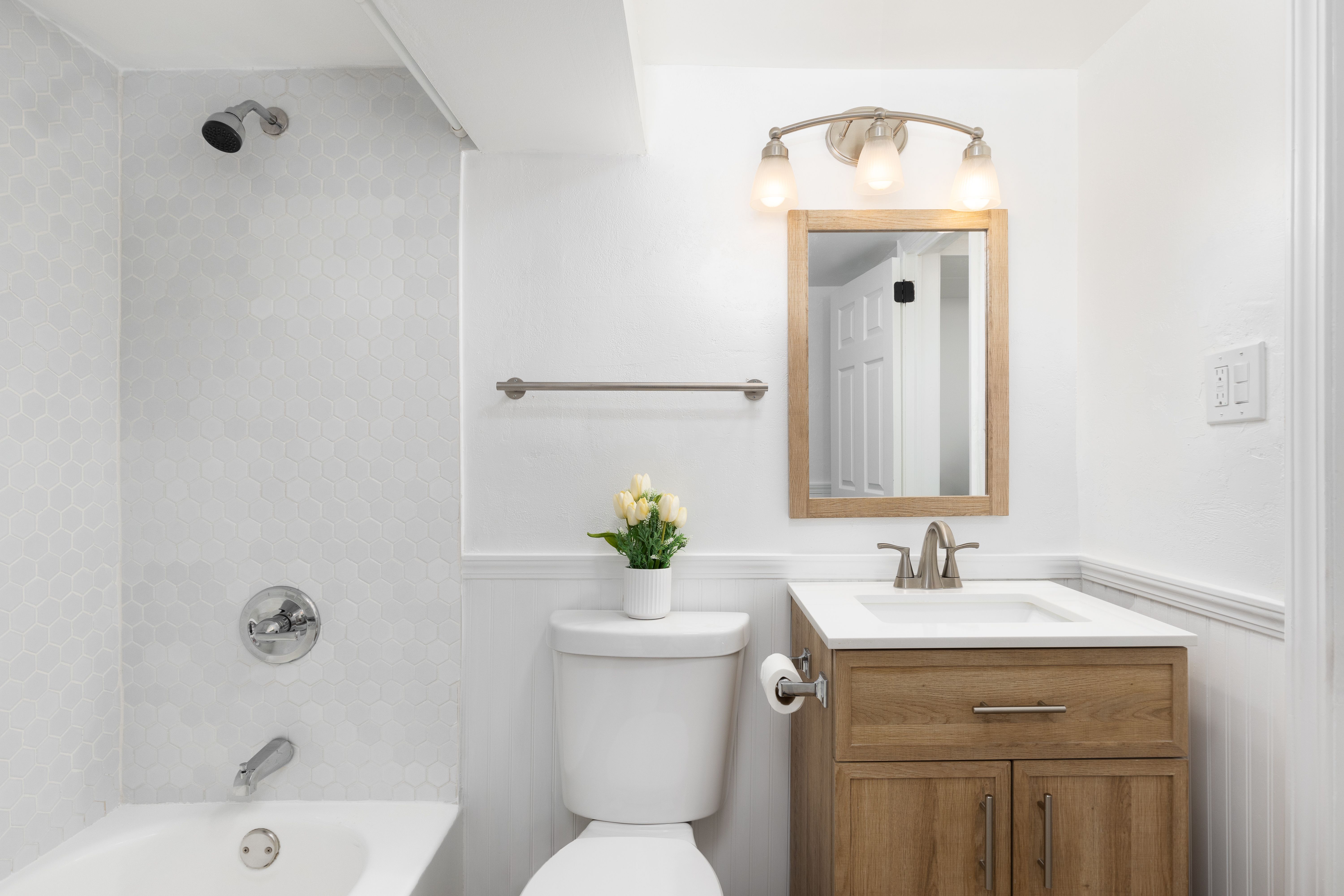 A bathroom with a wood cabinet and a hexagon tile shower.