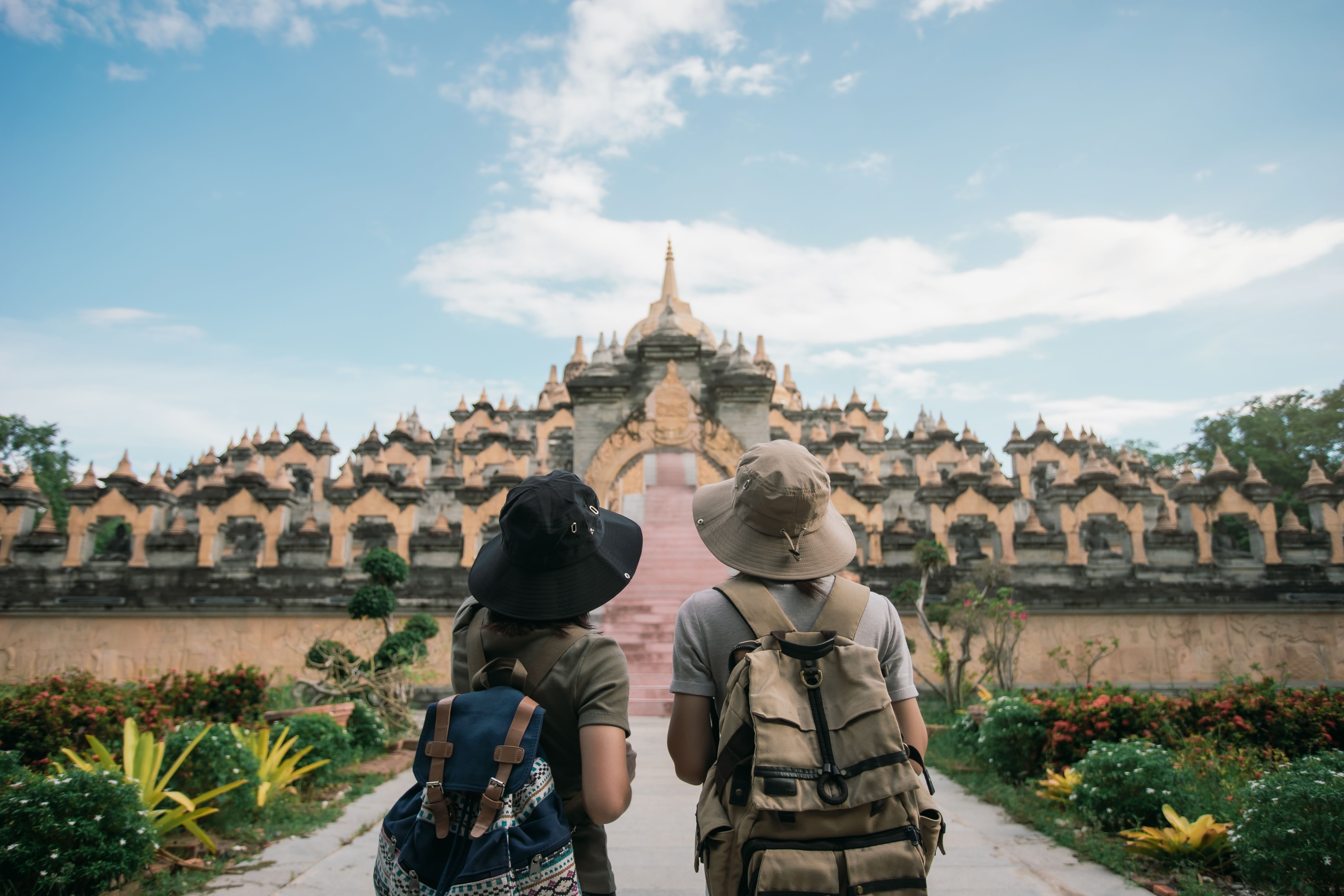 Behind two female traveler wearing a hat with backpack travel in the attraction architecture pagoda of buddhist culture in southeast Asia. Pagoda of Buddhist in Thailand.