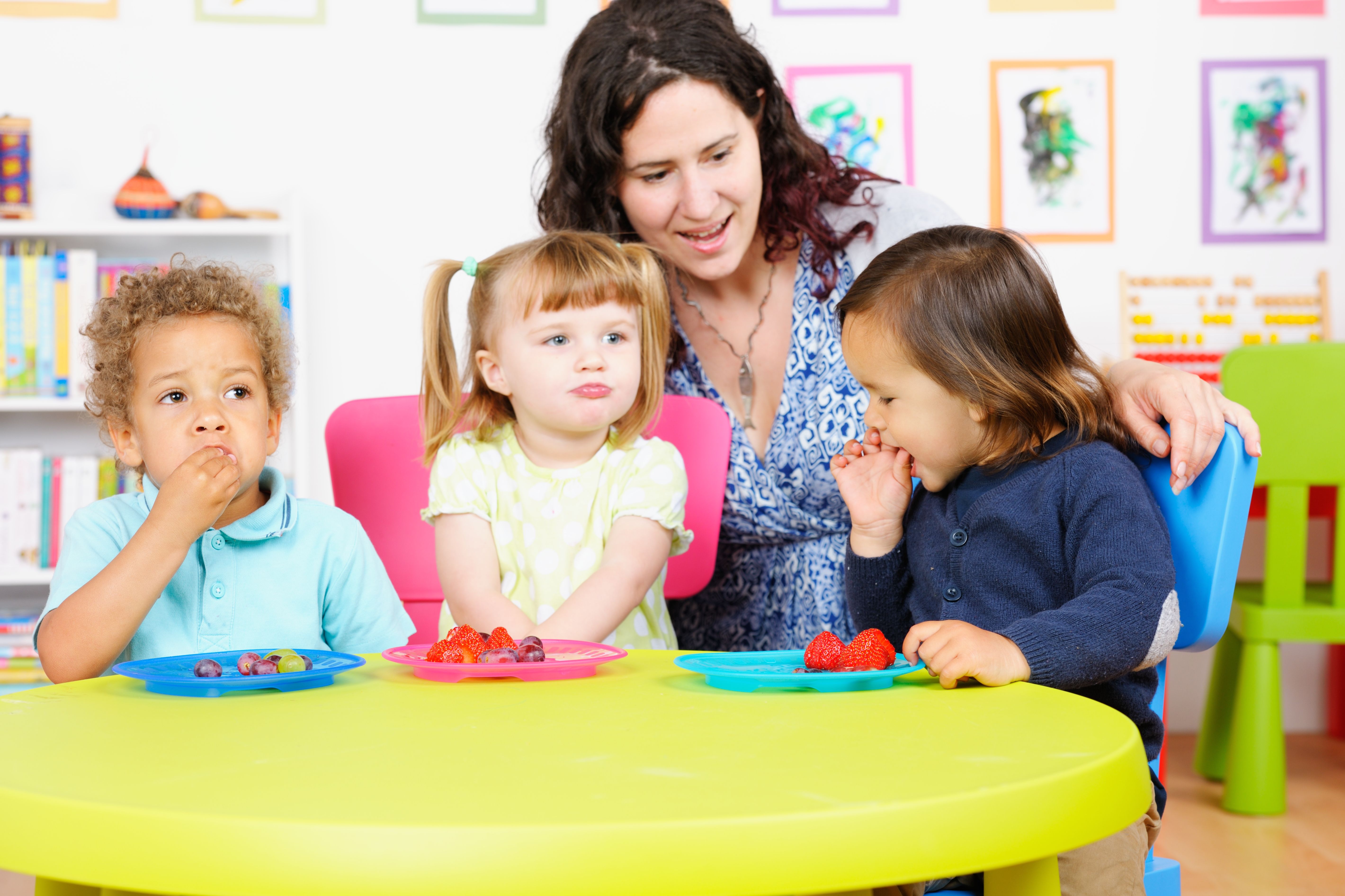 Carer With Group Of Little Children At Mealtime