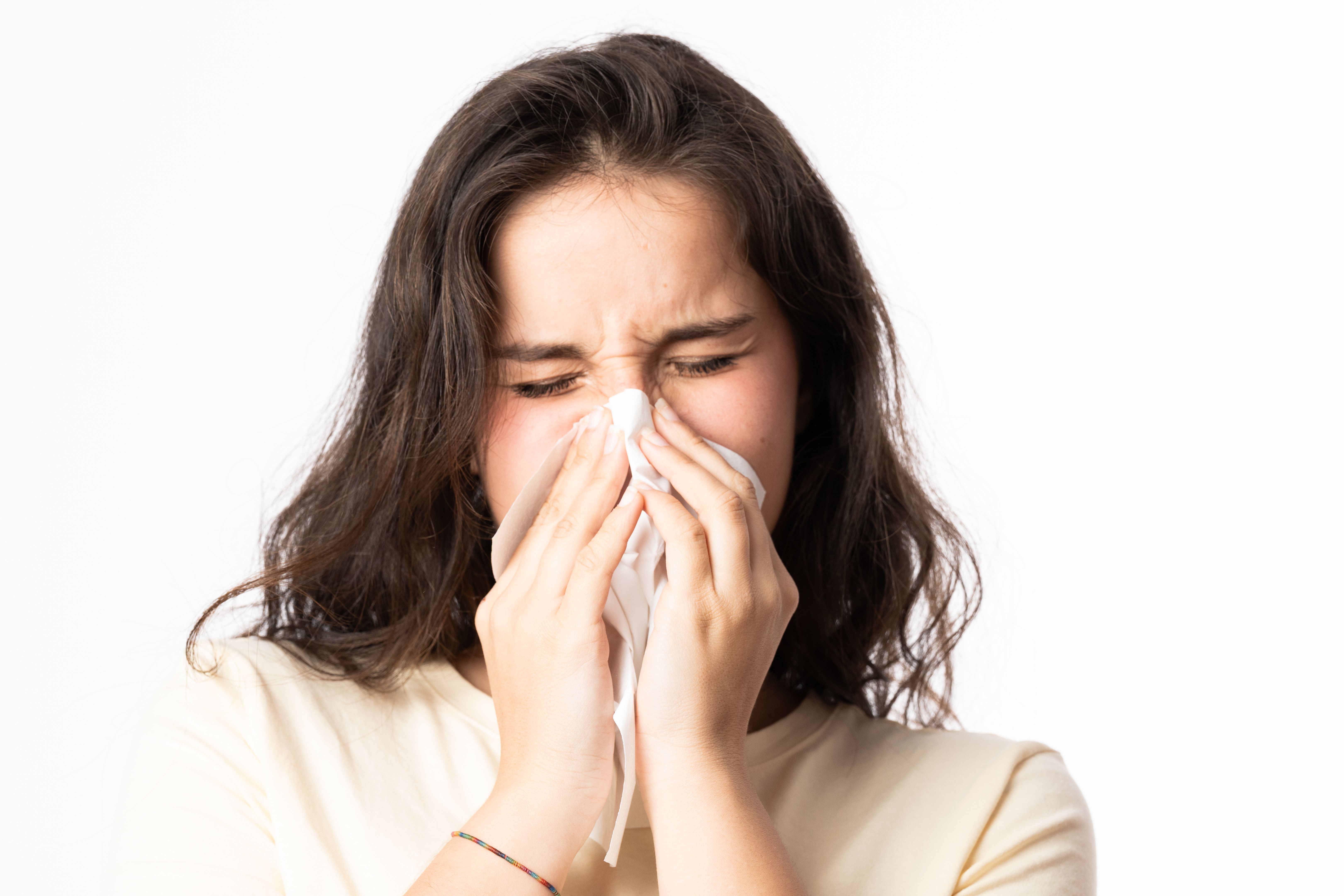 Young woman blowing her nose with tissue on white background