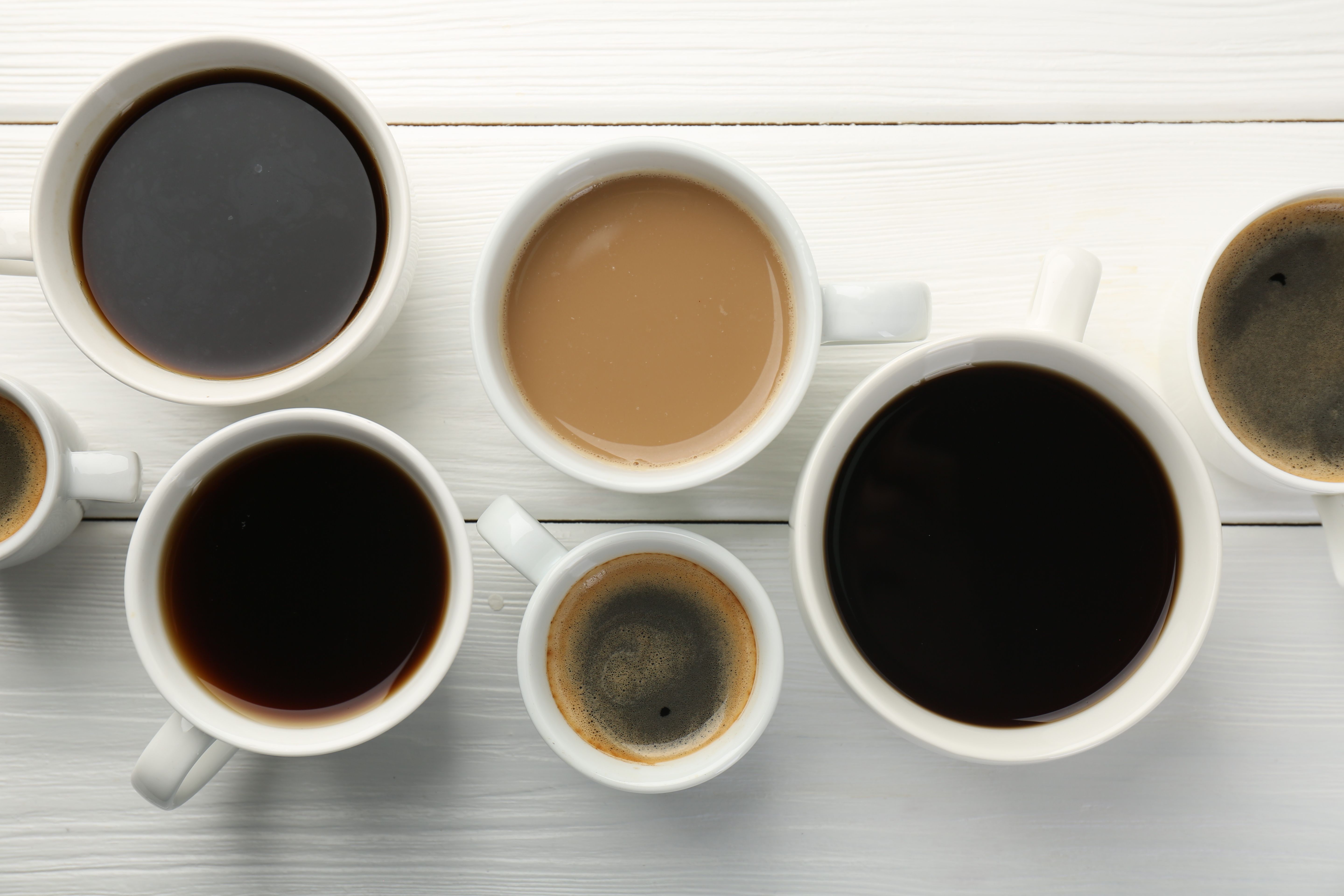 Different coffee drinks in cups on white wooden table, flat lay