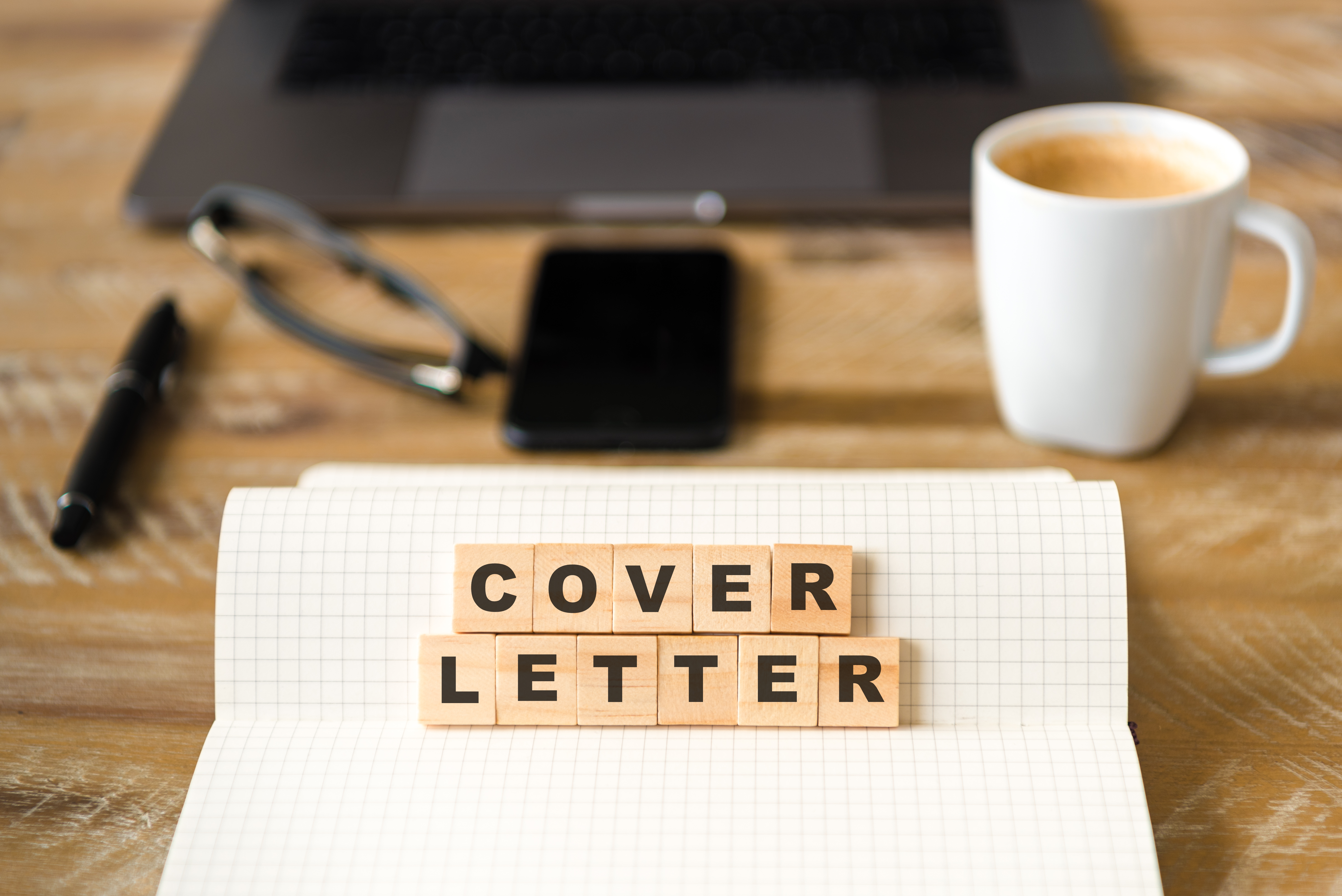 Closeup on notebook over wood table background, focus on wooden blocks with letters making COVER LETTER words Closeup on notebook over wood table background, focus on wooden blocks with letters making COVER LETTER words