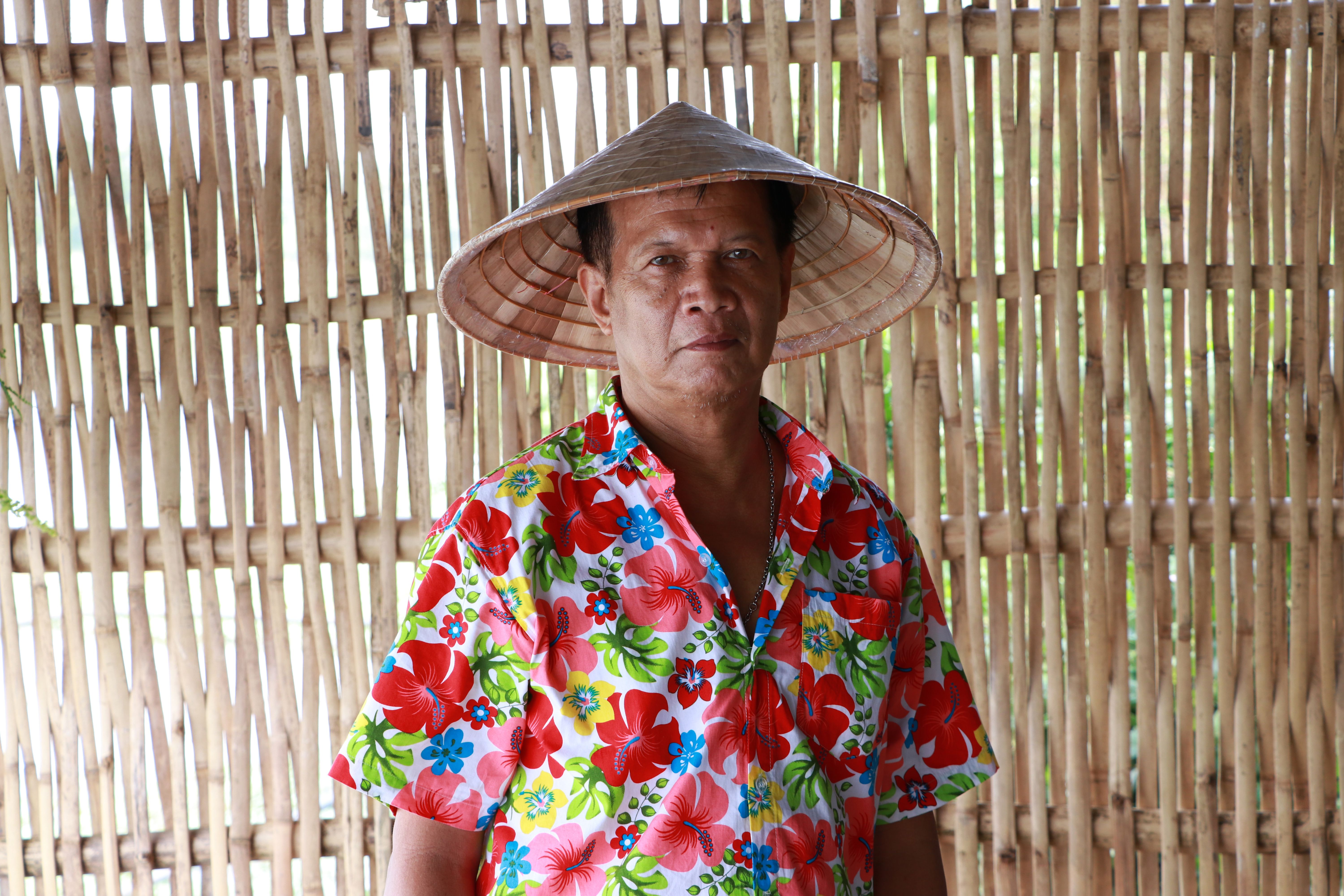 The man wearing a Vietnamese conical hat with a colorful floral pattern shirt.