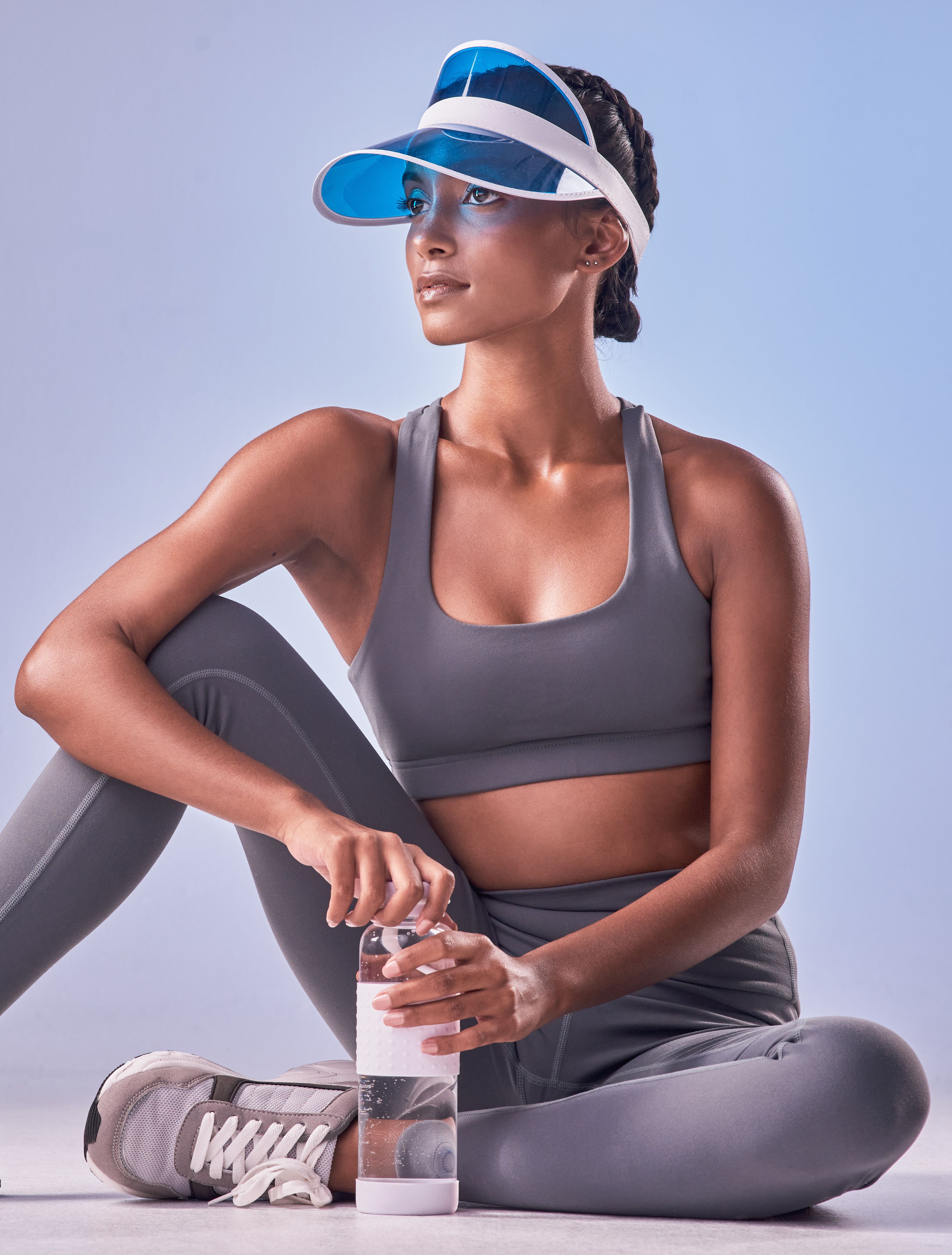 Studio shot of a fit young woman drinking bottled water against a grey background