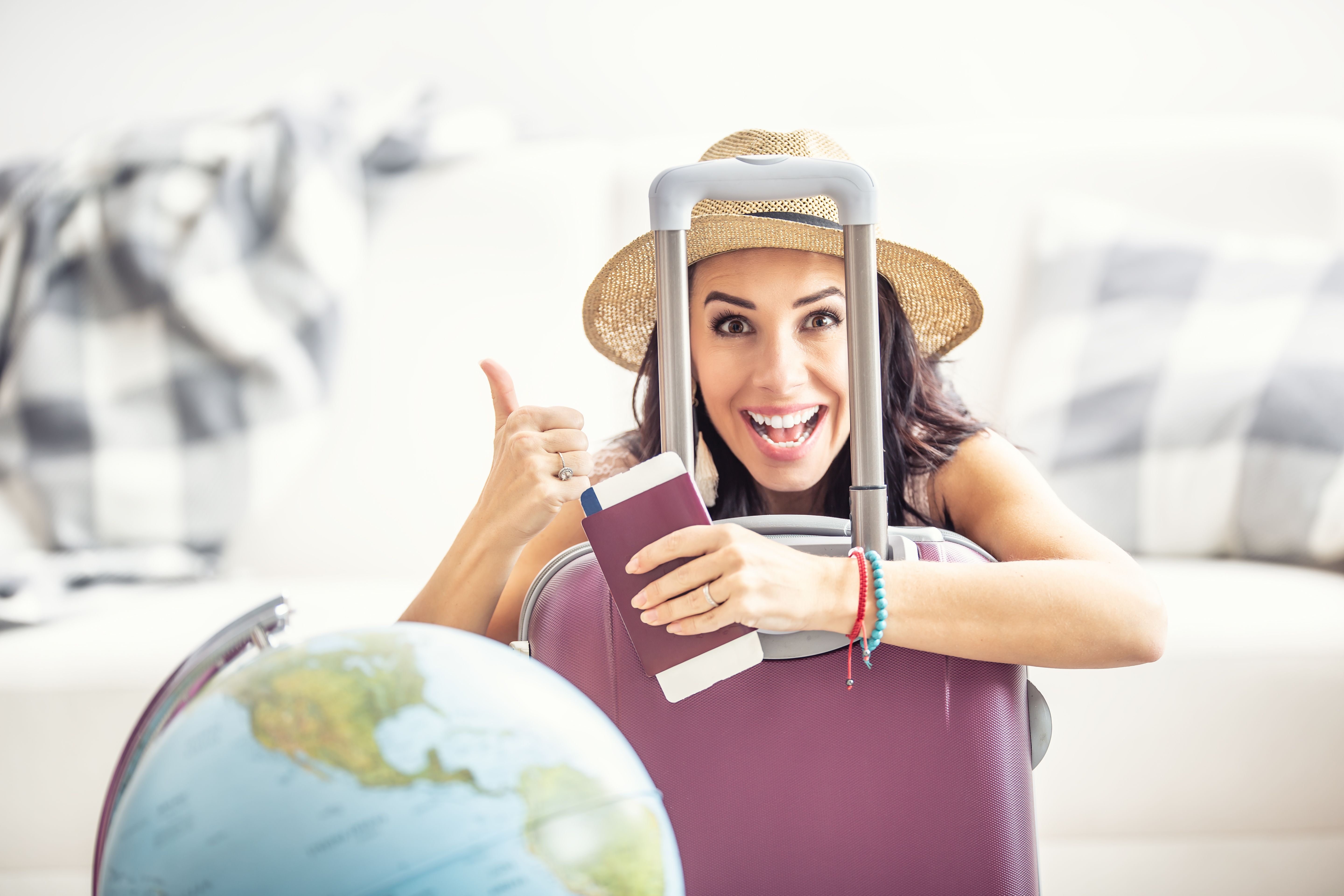 Excited woman with suitcase, passport, and globe giving a thumbs up.