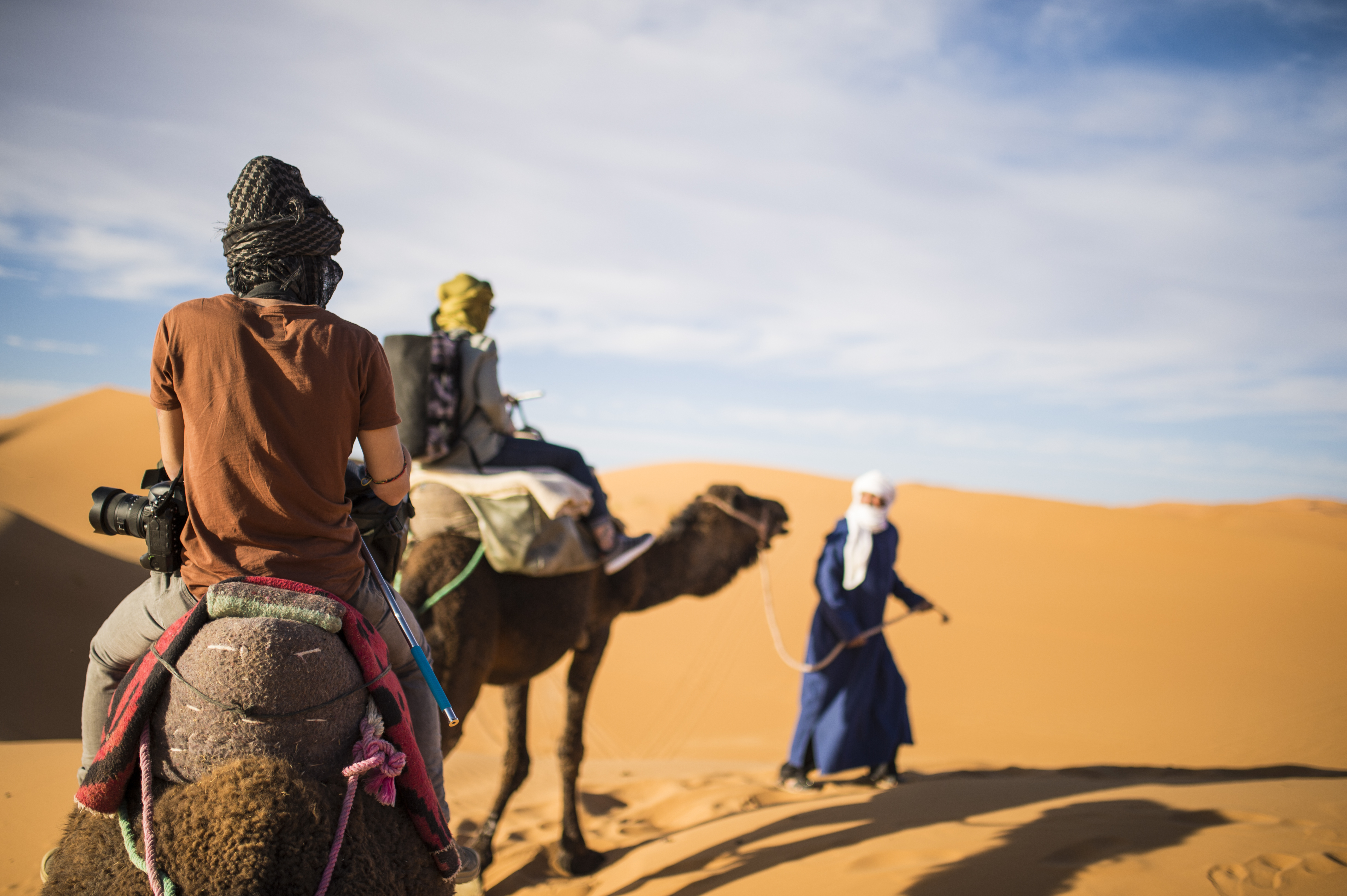 Tourists on camels going through the sand dunes in the Sahara Desert at sunset - Morocco.