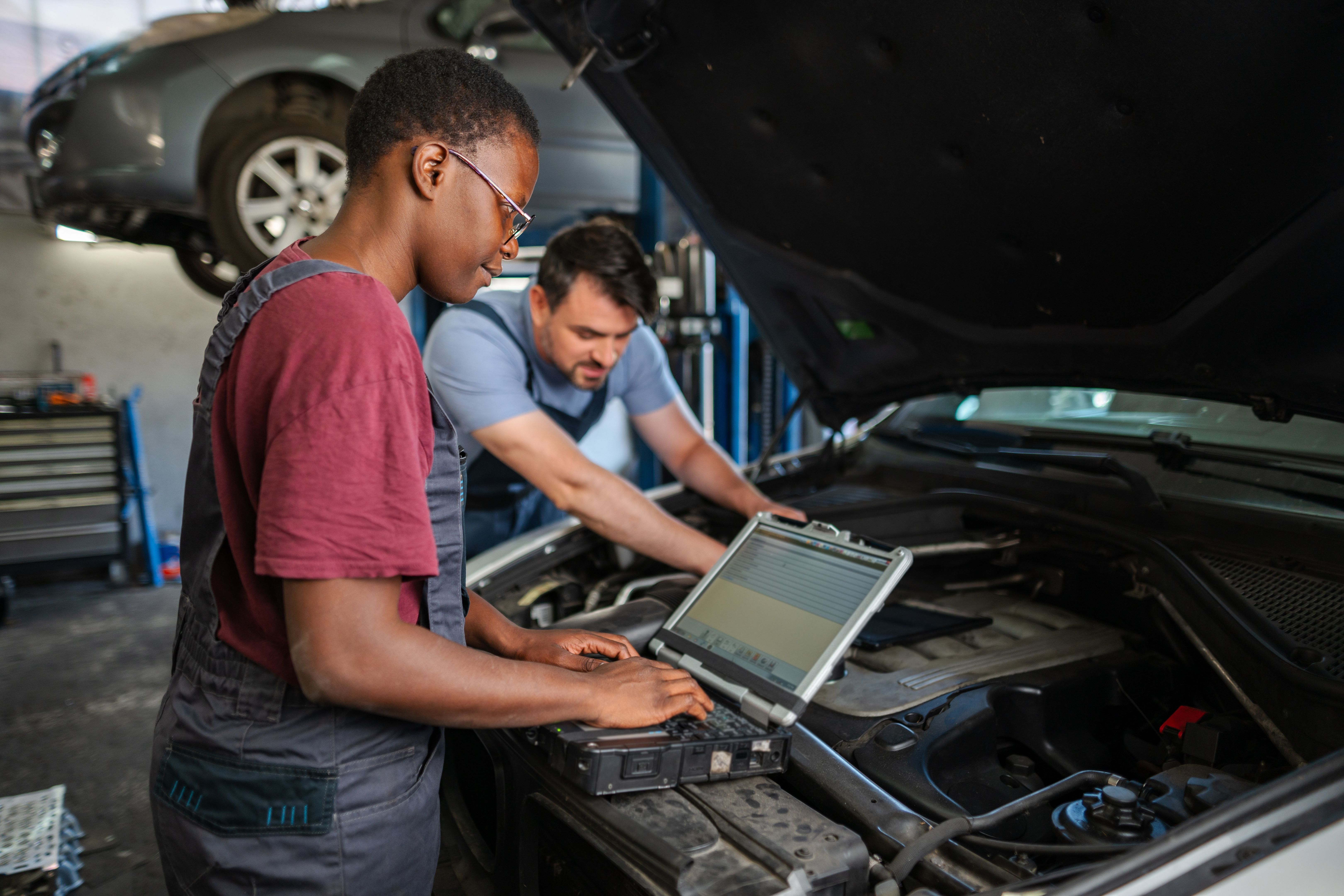 Mechanics using diagnostic software on laptop are examining car engine