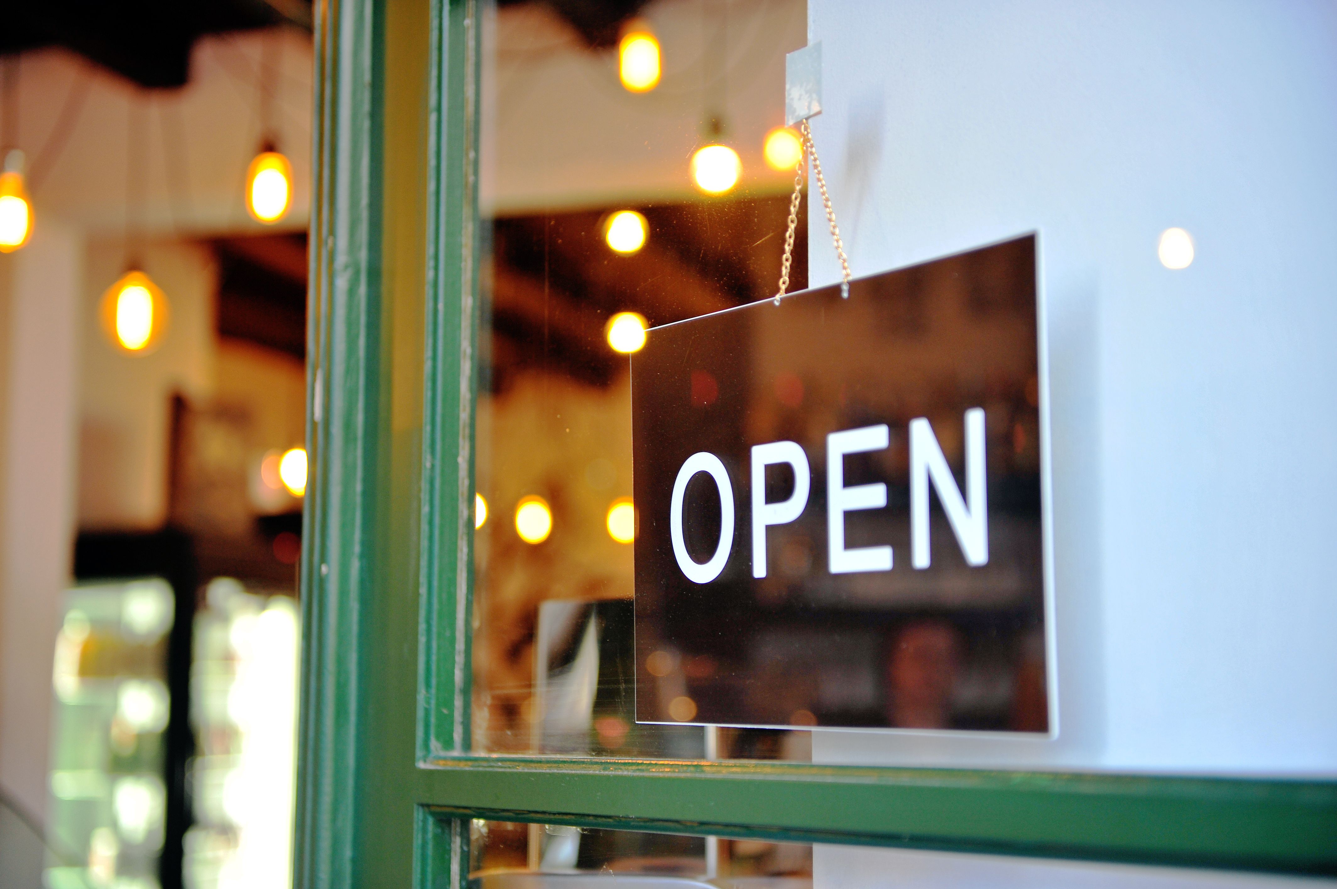 Black hanging open sign in the green wooden door of retail store, business background