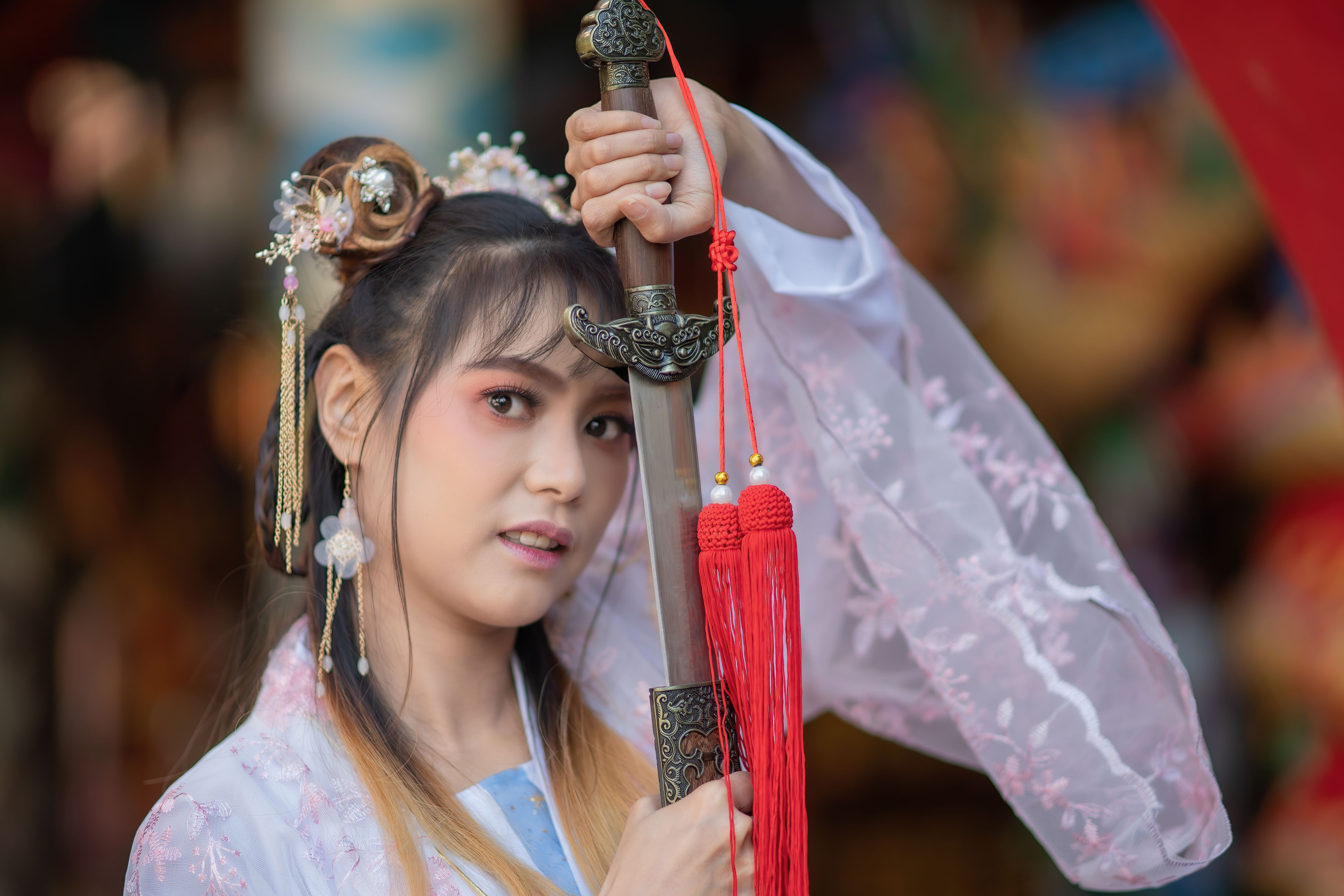 Asian woman wearing traditional Chinese dress pink white color holding Chinese sword