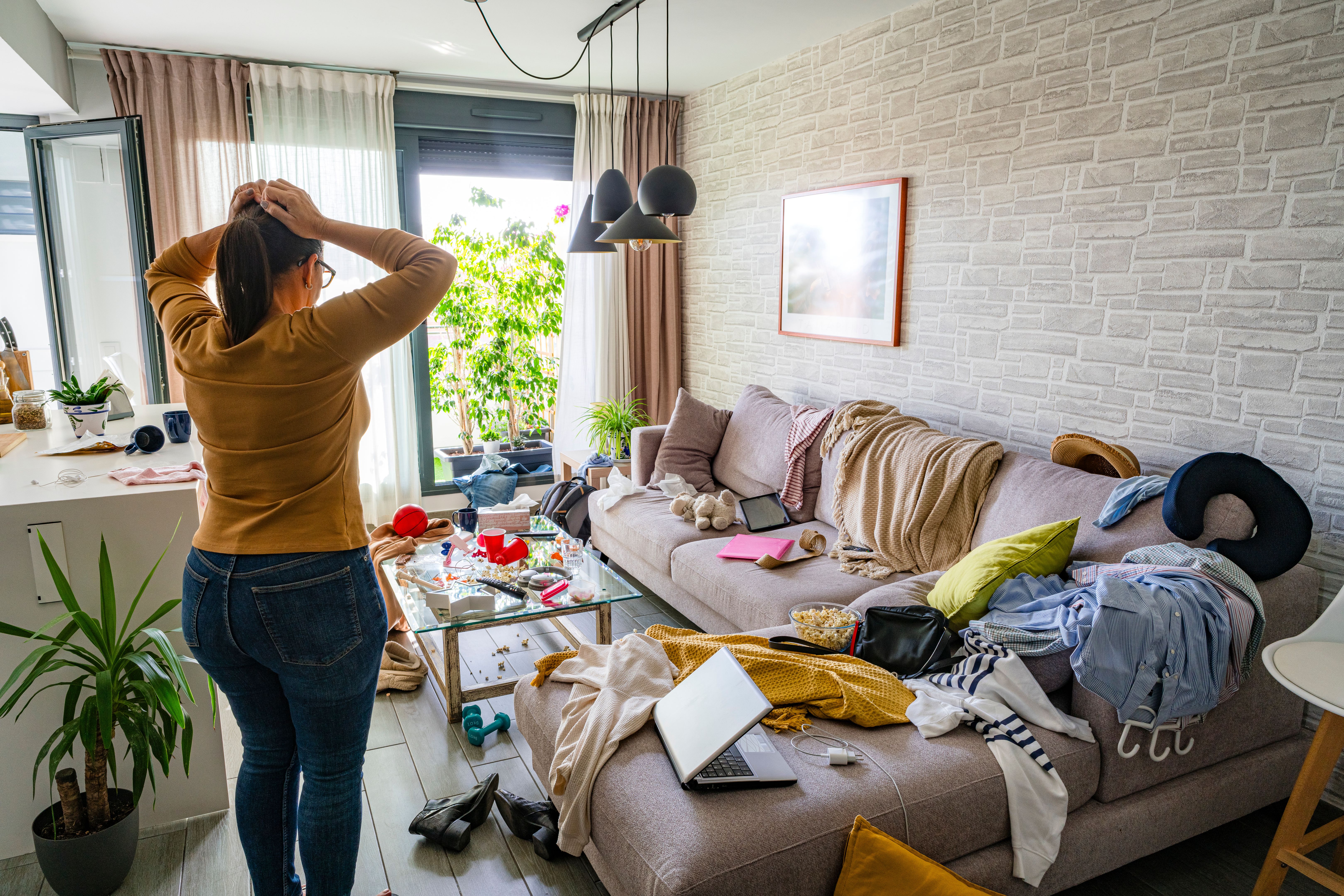 Upset woman head in hands contempling her messy and dirty living room