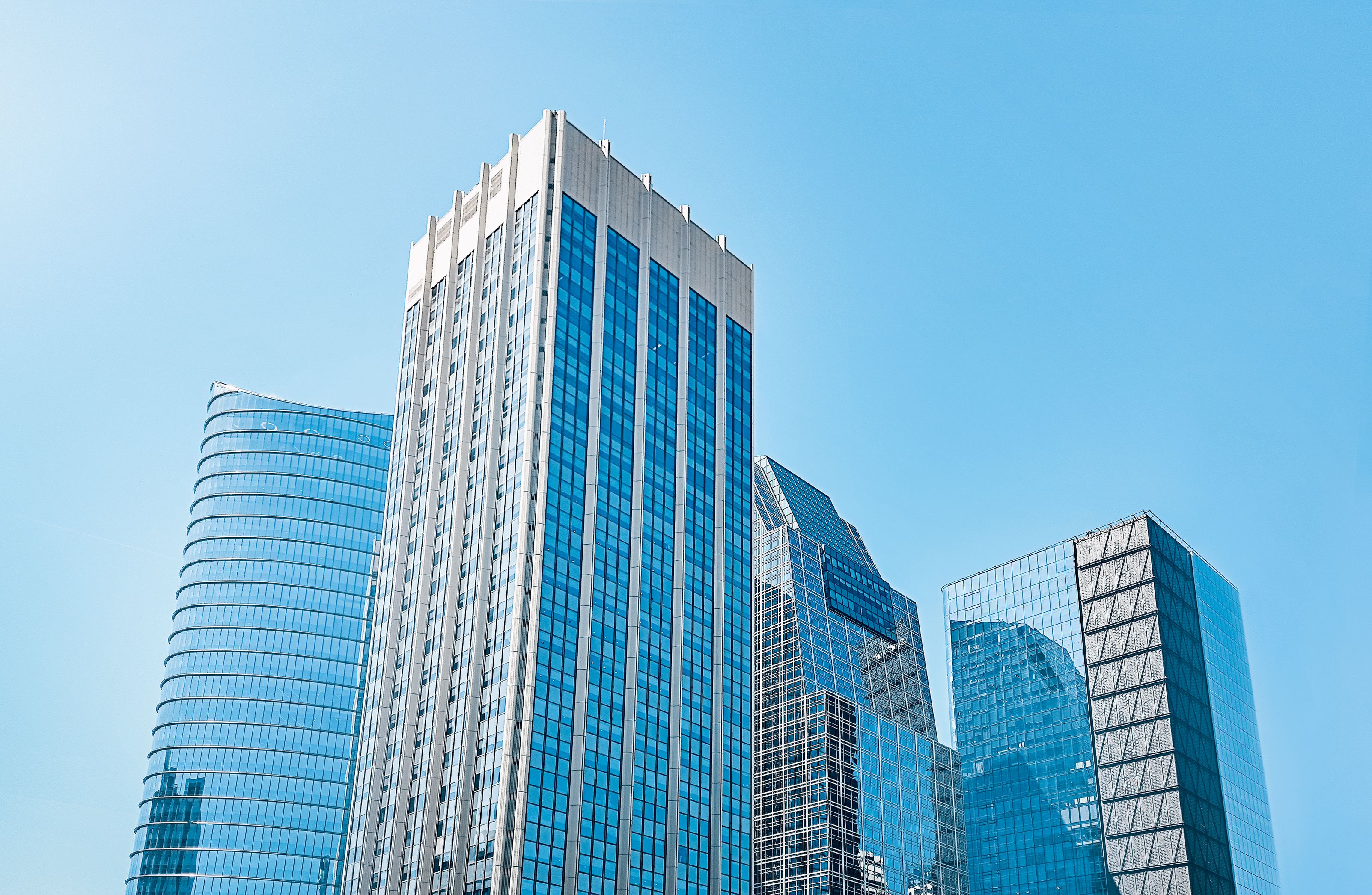 Four high-rise buildings with mirrored windows against a clear blue sky