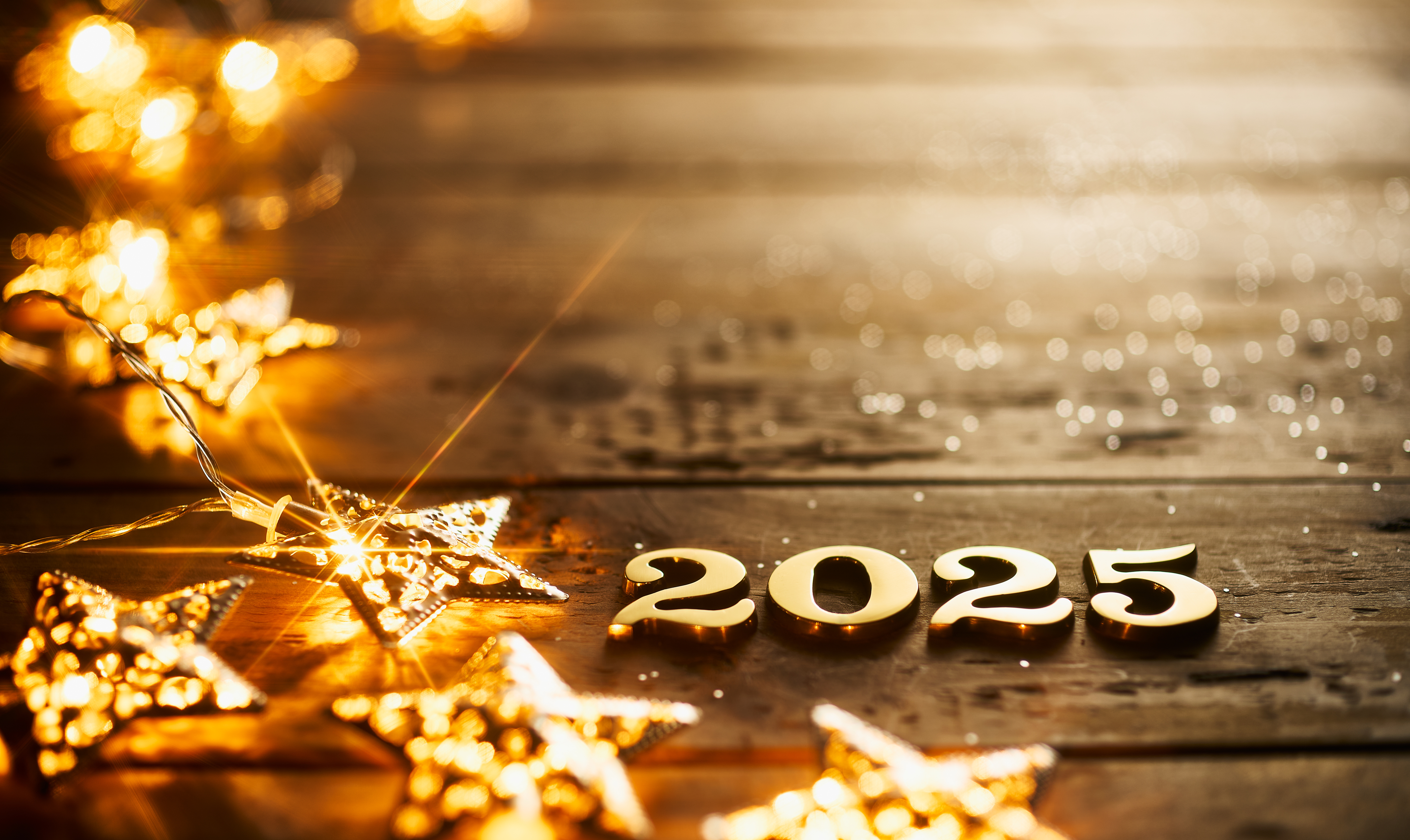 Glowing golden 2025 numbers with festive star-shaped fairy lights on rustic wooden surface, celebrating the New Year with warm ambiance.