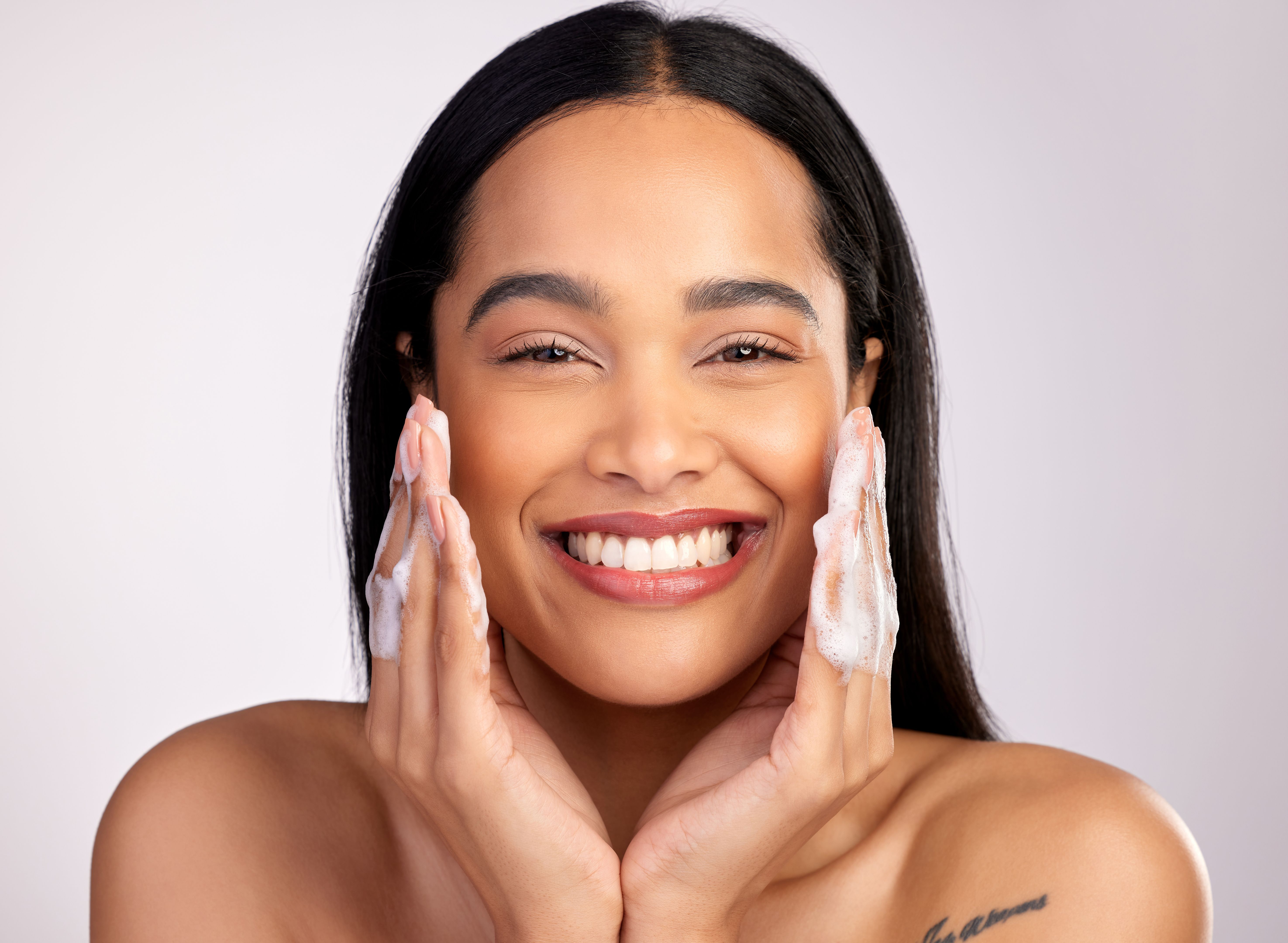 Studio portrait of an attractive young woman washing her face against a pink background Studio portrait of an attractive young woman washing her face against a pink background
