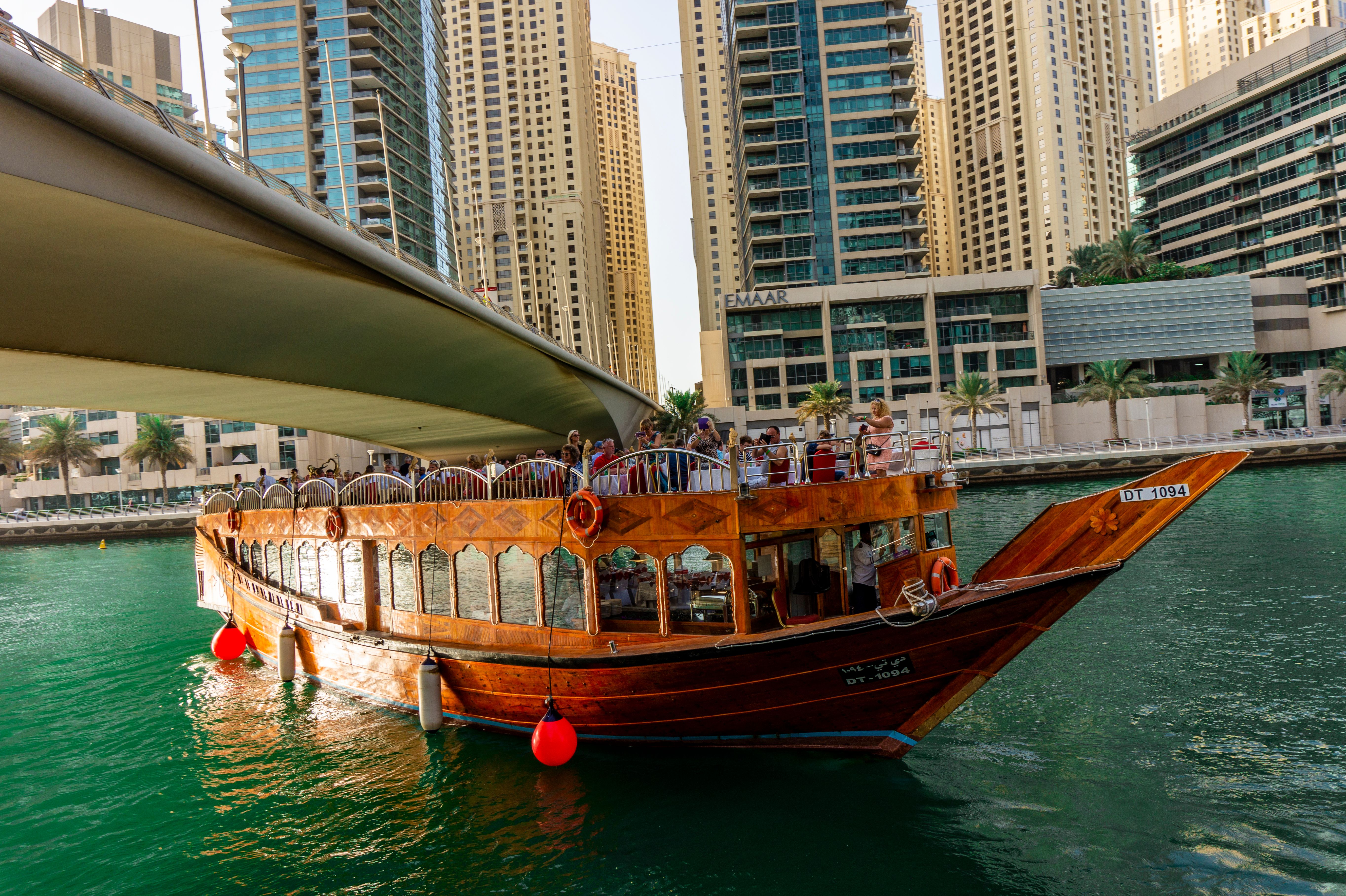 Famous traditional wooden old dhow cruise tour in the marina with tourist on the board and modern skyscrapers