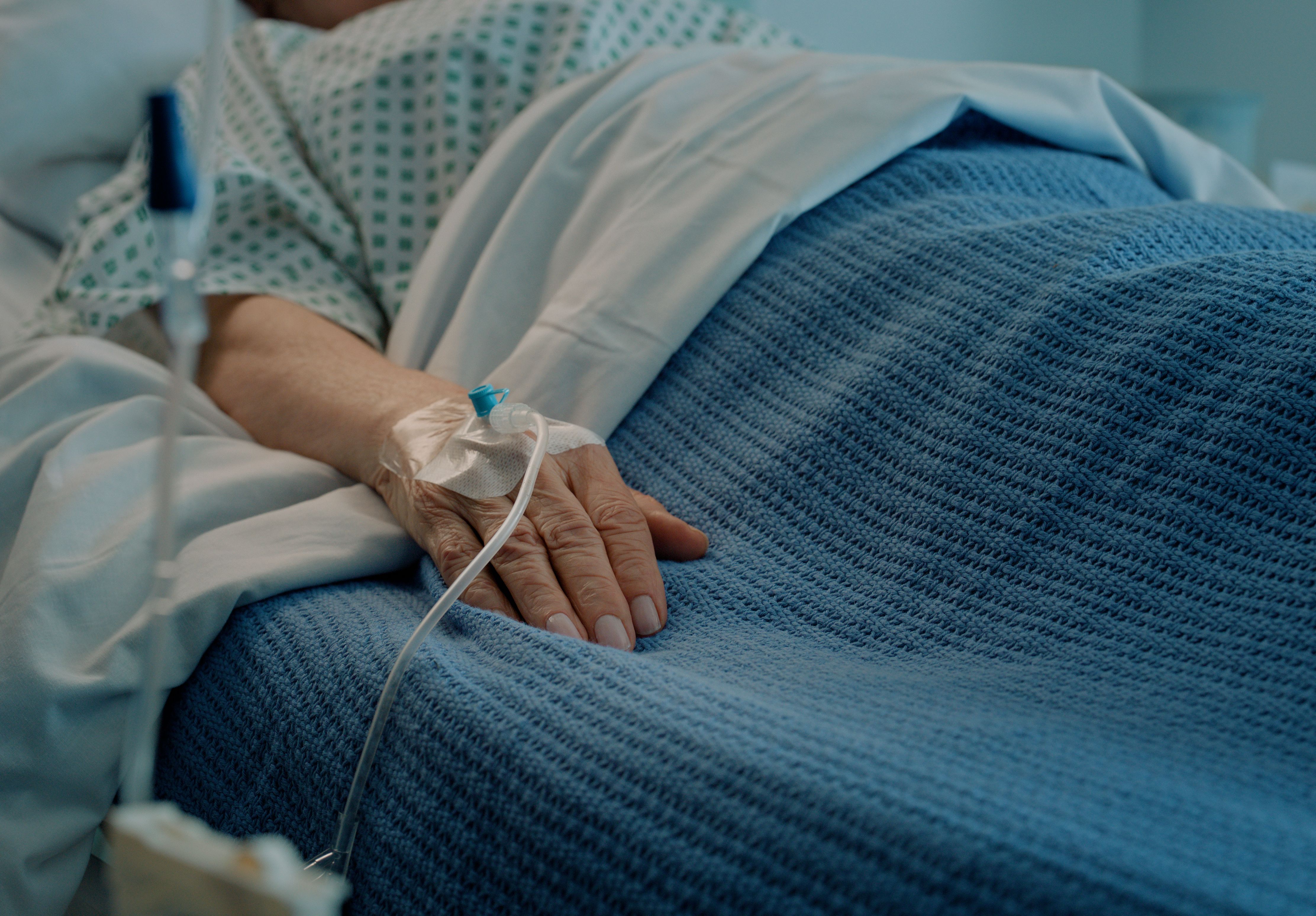 IV drip, tube and hand of patient in hospital, clinic and healthcare facility for health, wellness or healing. Bed, senior person and medical equipment for intensive care, life support and medicine