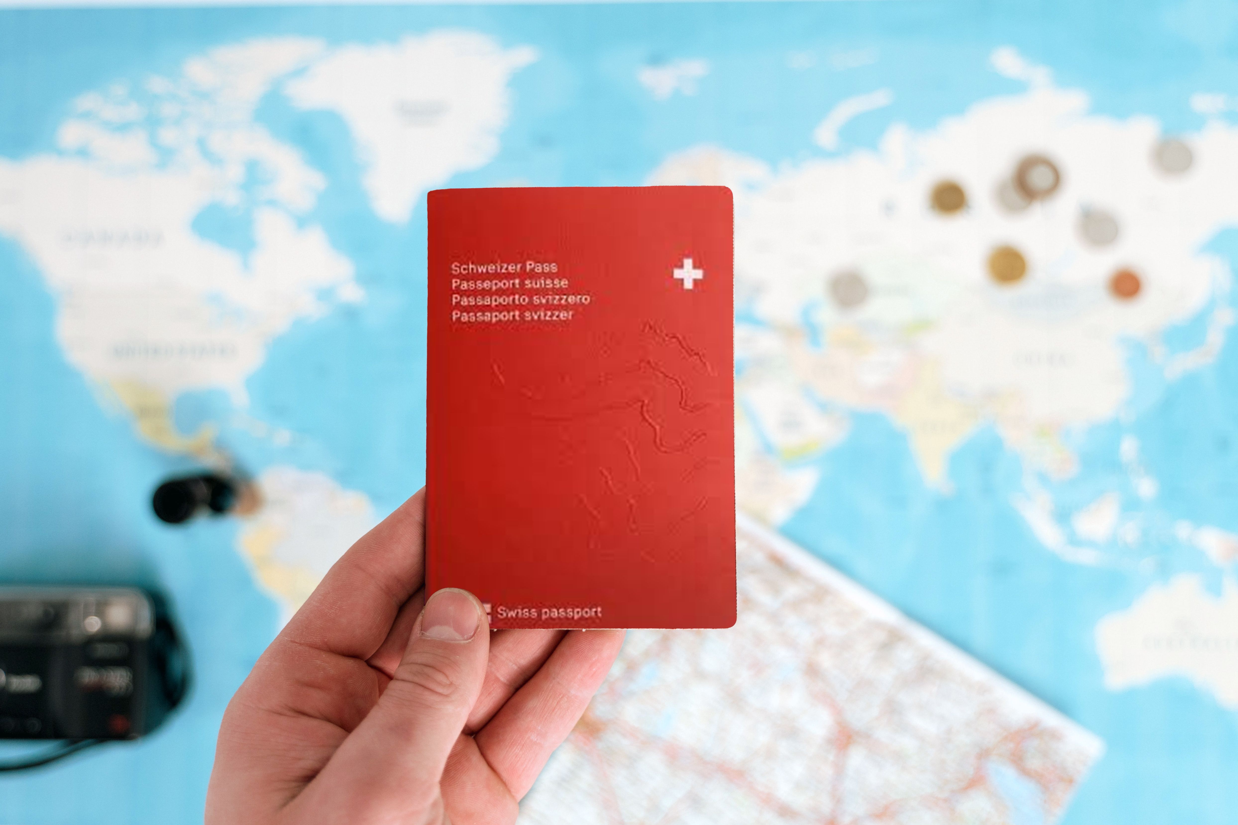 Passeport suisse tenu en main avec une carte en arrière-plan.