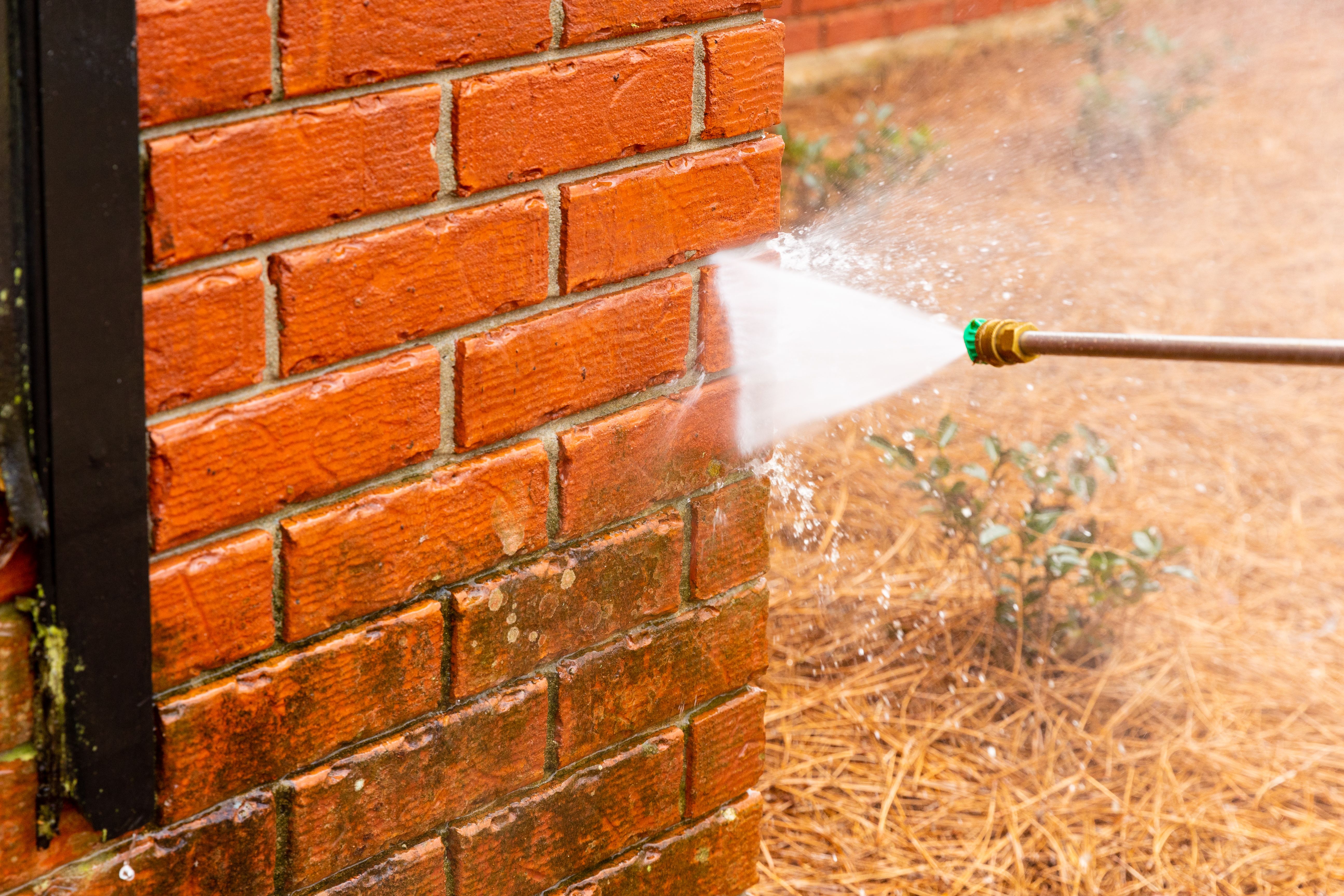 Dirty brick wall being cleaned with a pressure washer.