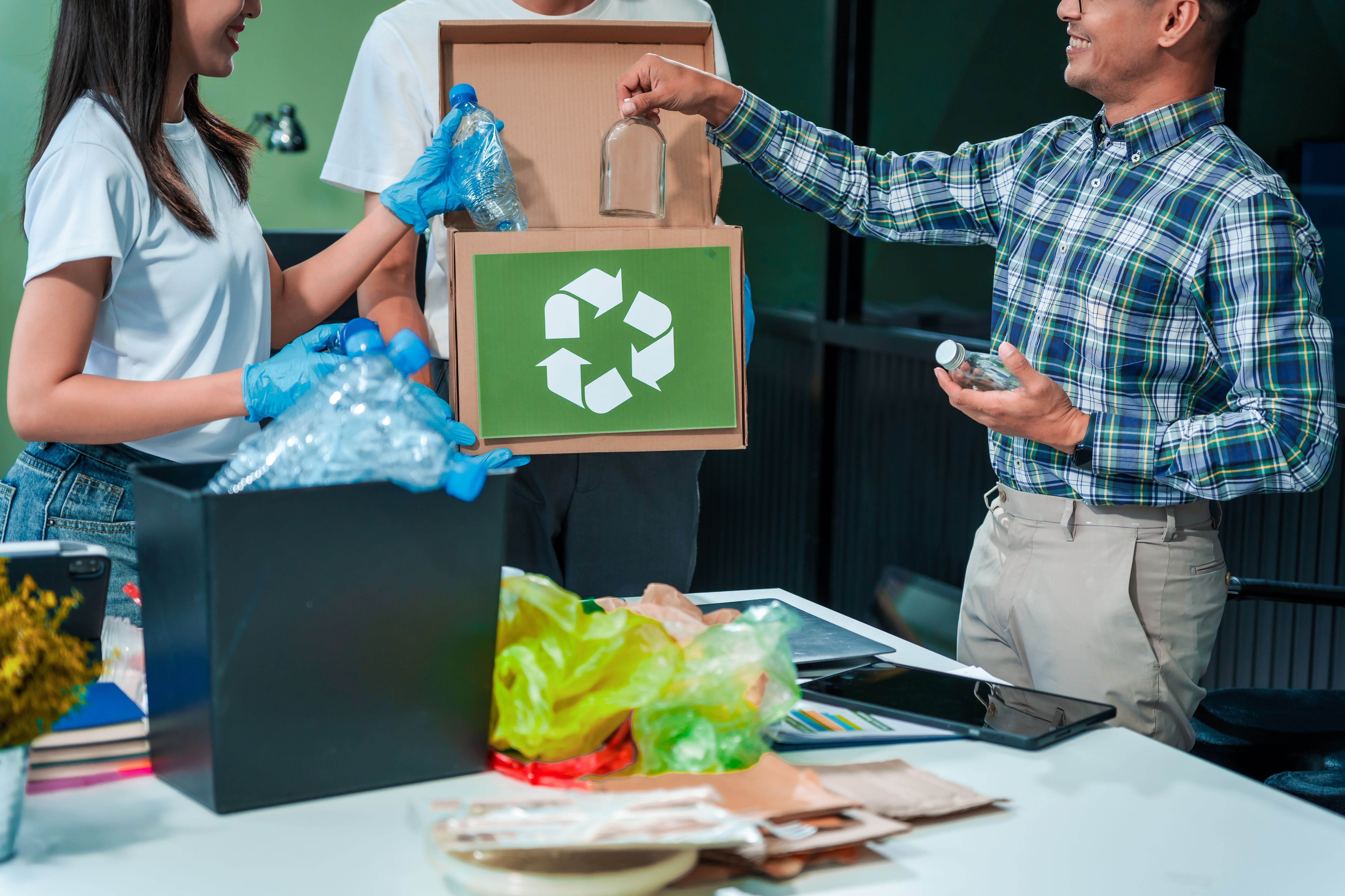 In an office, an Asian team discusses waste management strategies at a desk, separating plastic waste. They explore recycling systems and zero-waste goals to improve environmental sustainability. In an office, an Asian team discusses waste management strategies at a desk, separating plastic waste. They explore recycling systems and zero-waste goals to improve environmental sustainability.
