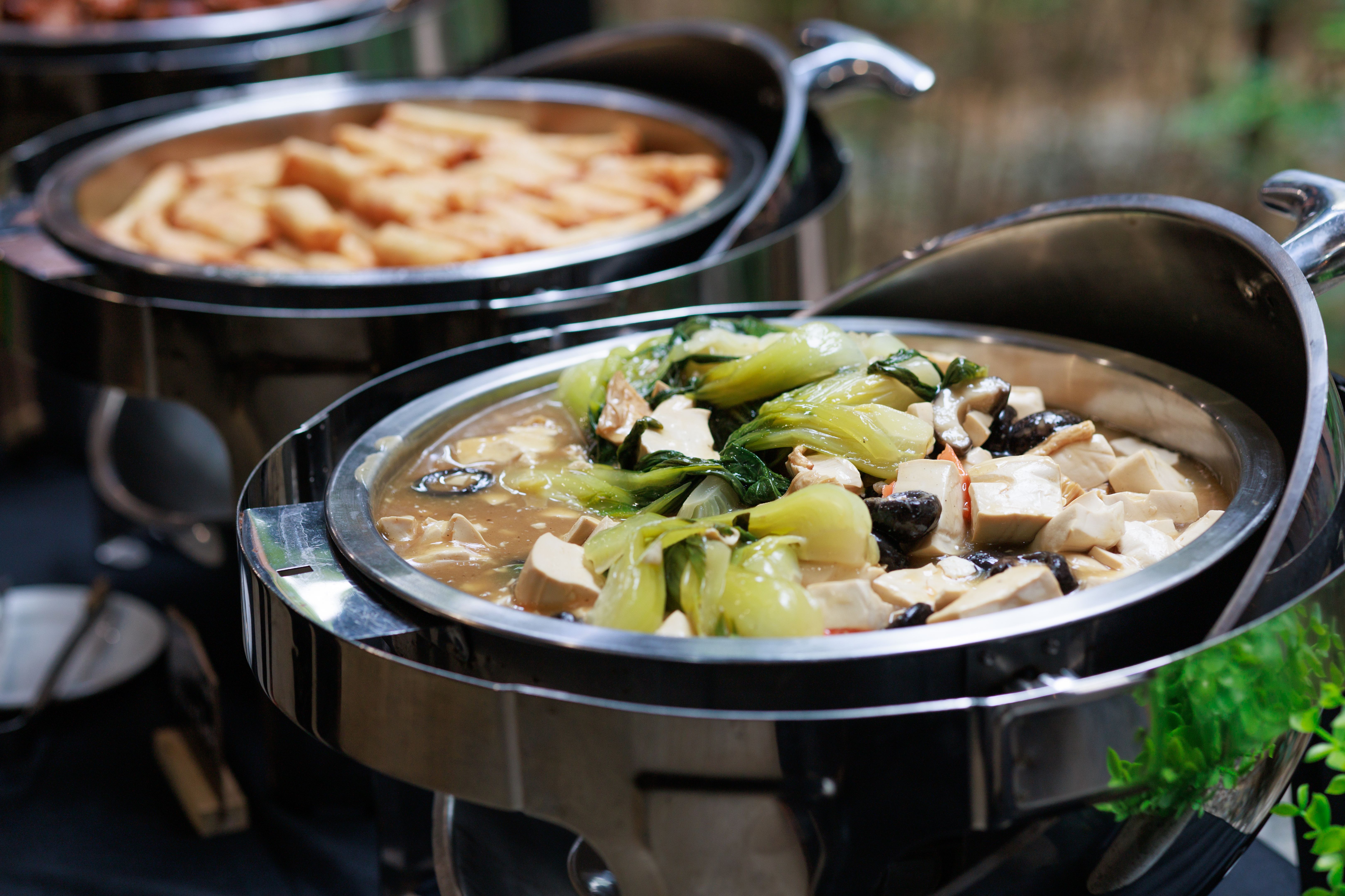 A variety of Asian food is displayed in chafing dishes on a buffet table, offering a diverse and tempting selection for diners.