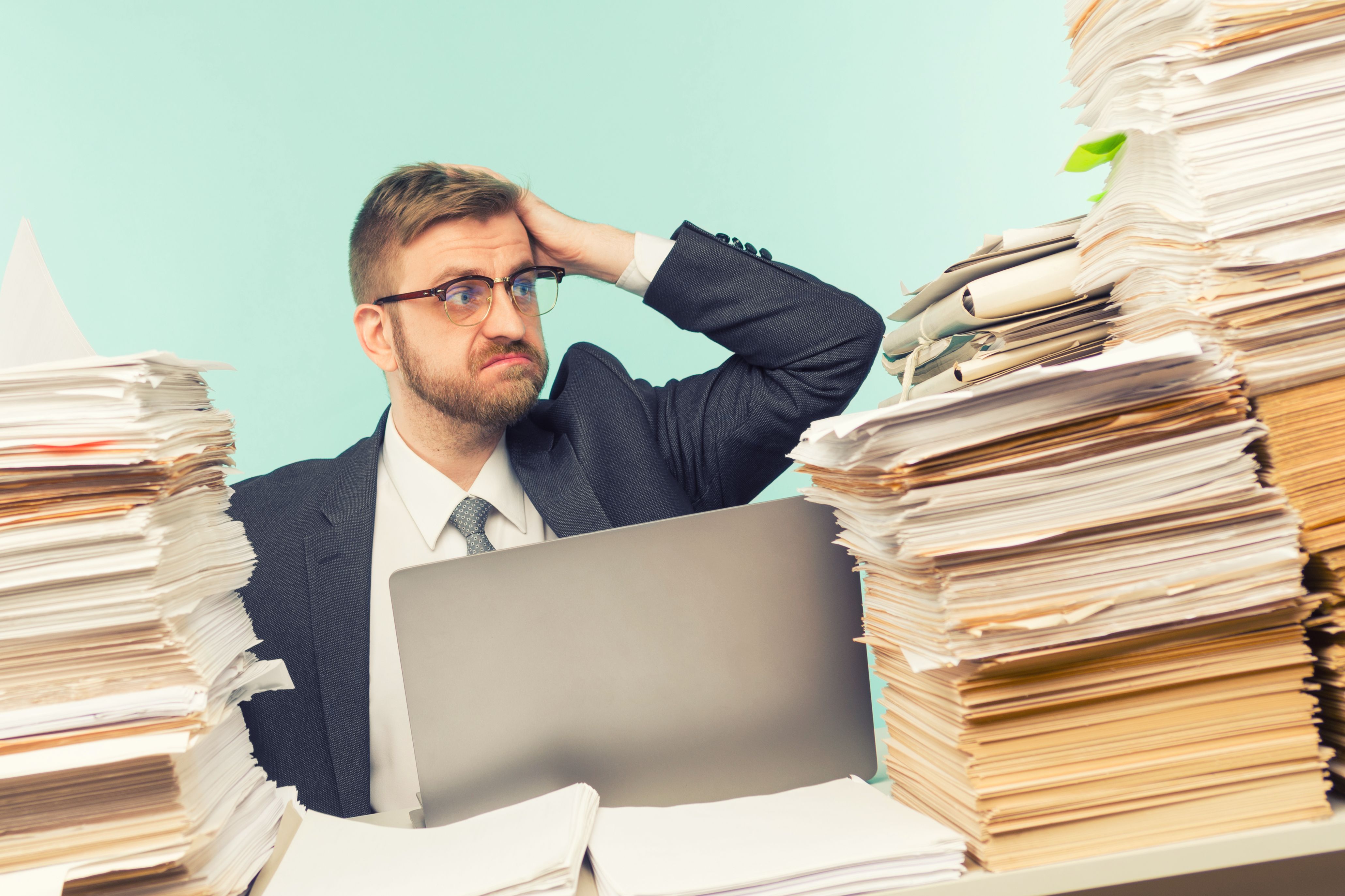 Shocked businessman sitting at the table with many papers in office Shocked businessman sitting at the table with many papers in office
