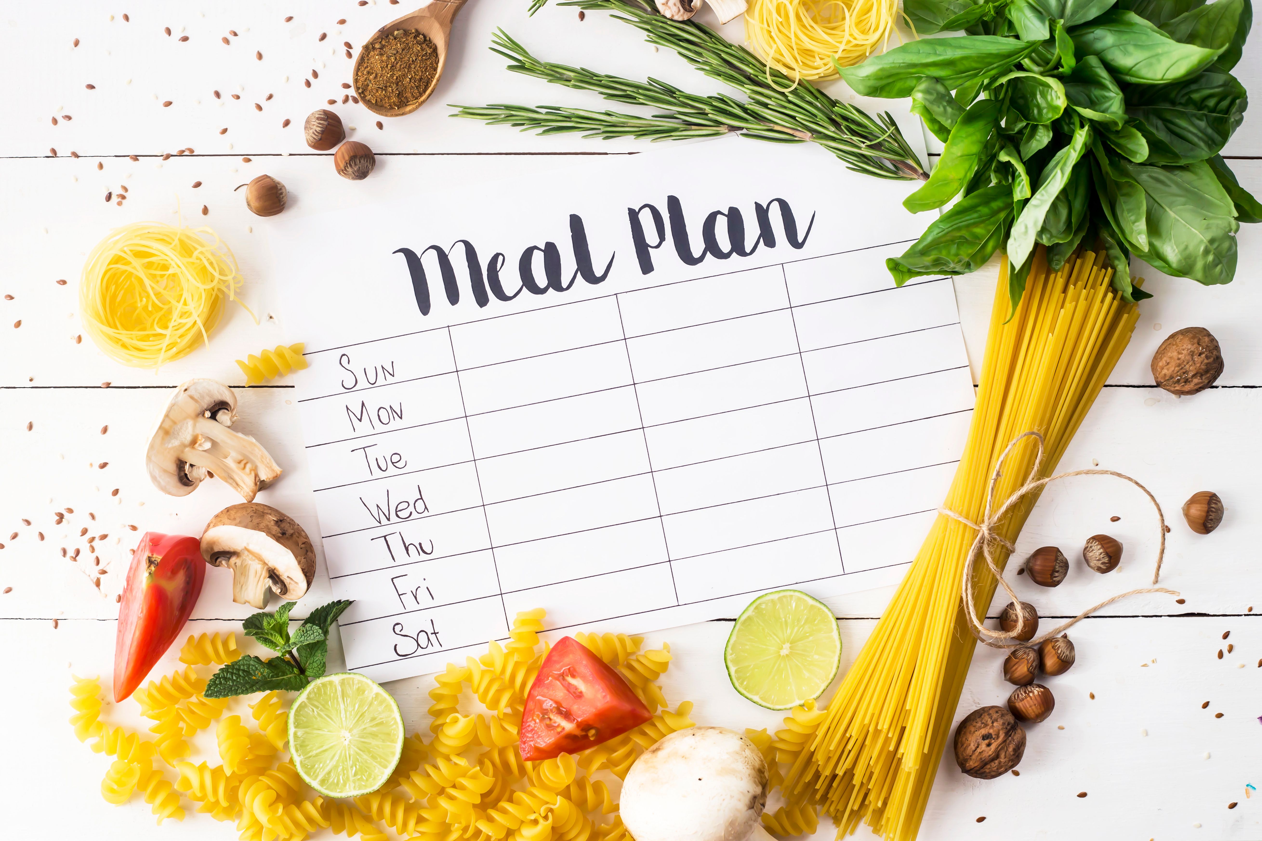 A meal plan for a week on a white table among products for cooking - pastas, basil, vegetables, lime, seeds, nuts and spices. Top view, flat lay, copyspace A meal plan for a week on a white table among products for cooking - pastas, basil, vegetables, lime, seeds, nuts and spices. Top view, flat lay, copyspace