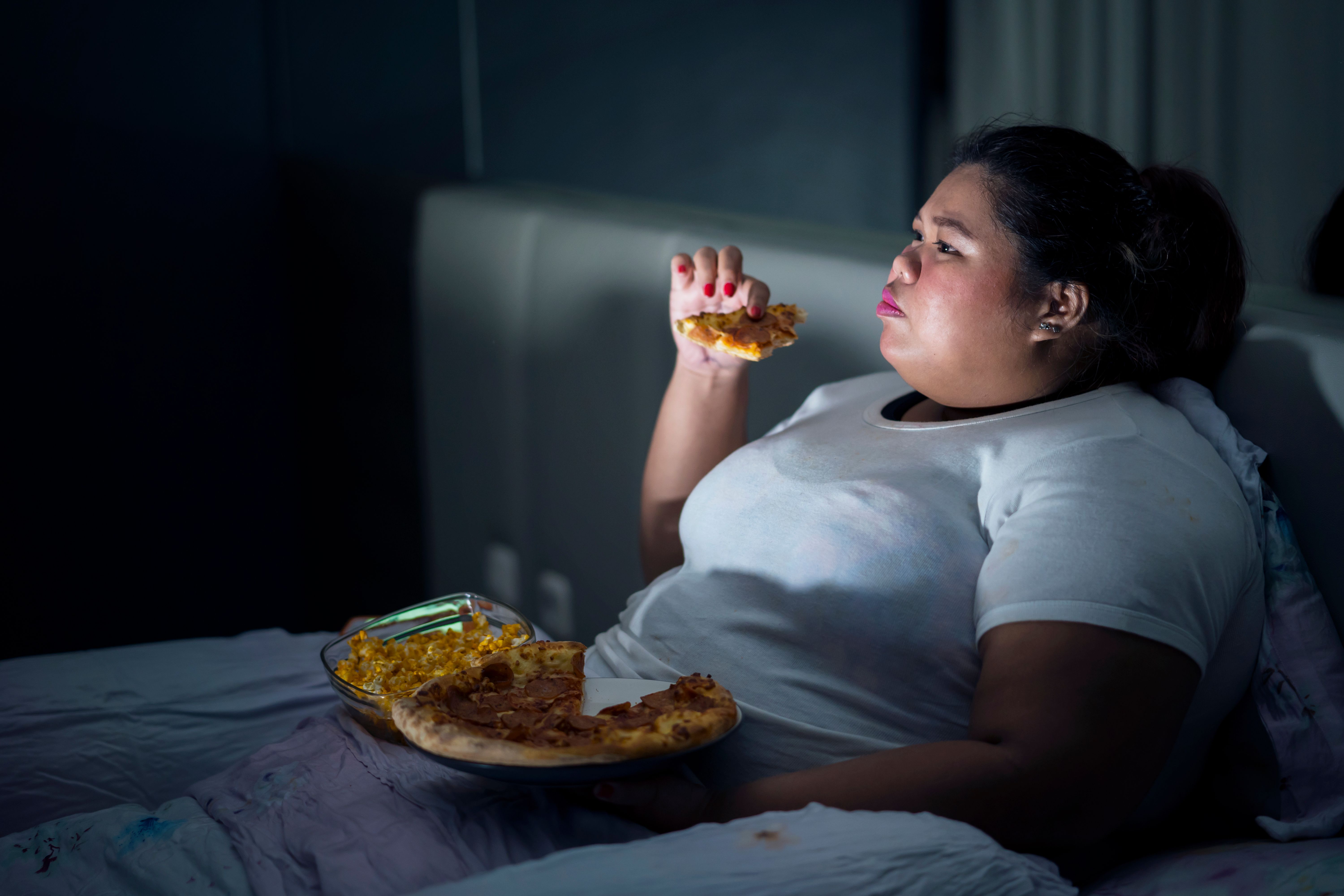 Fat woman eating pizza on bed Fat woman eating pizza on bed