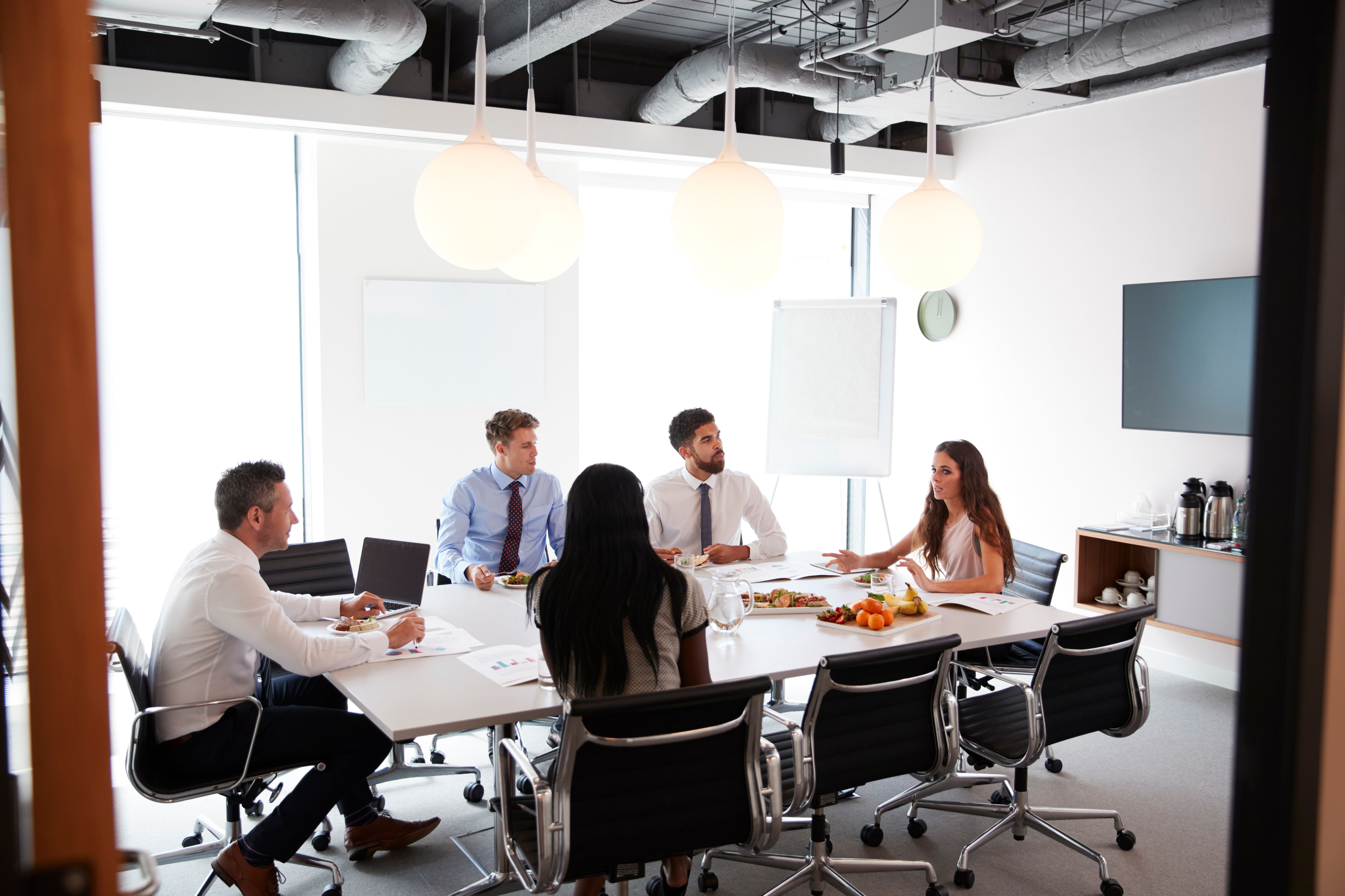 Businessmen And Businesswomen Meeting In Modern Boardroom Over Working Lunch