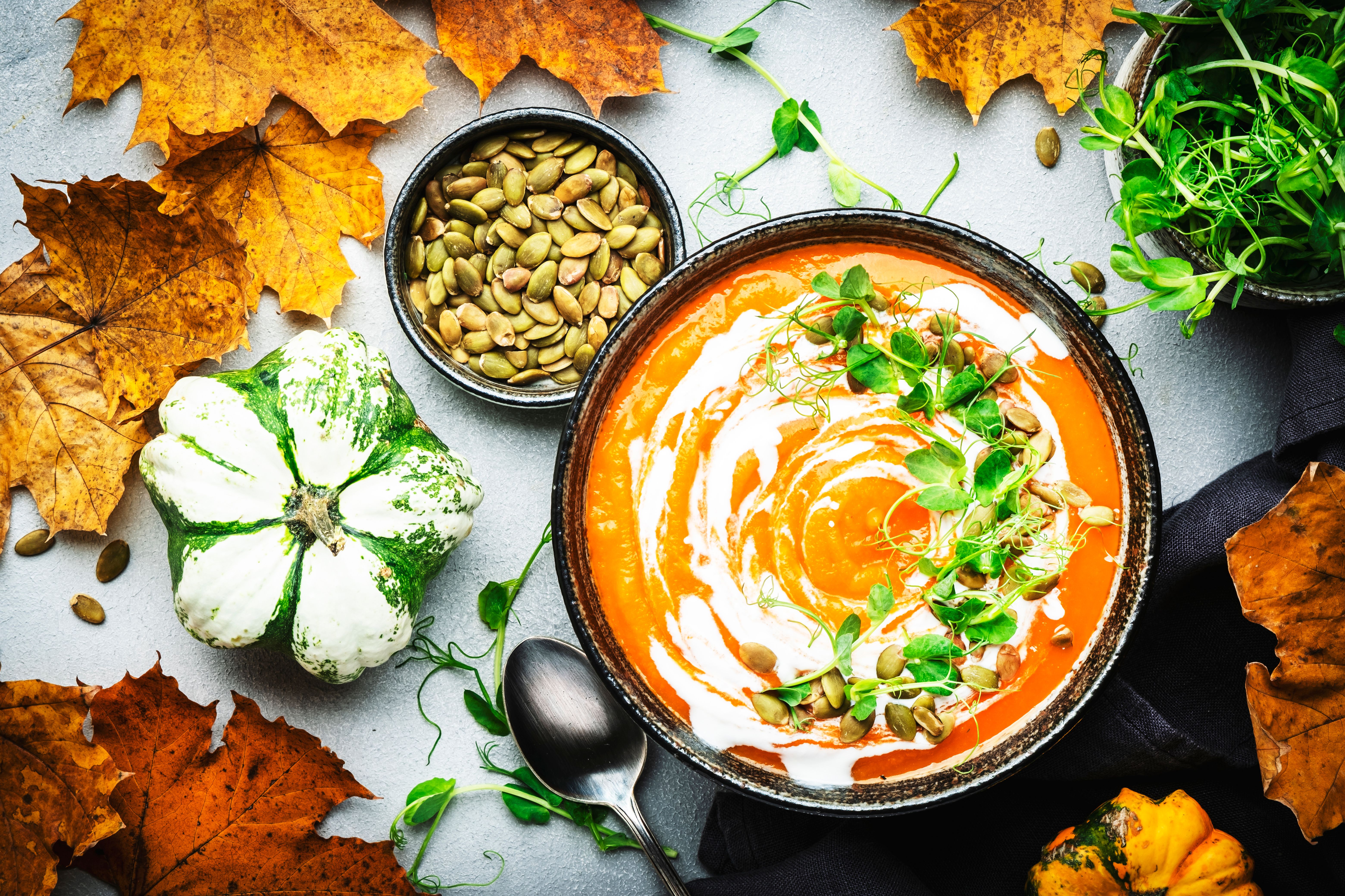 Vegan pumpkin carrot  soup with pumpkin seeds, coconut cream and pea sprouts. Winter or autumn healthy vegetarian slow food. Soup bowl on gray table background. Top view