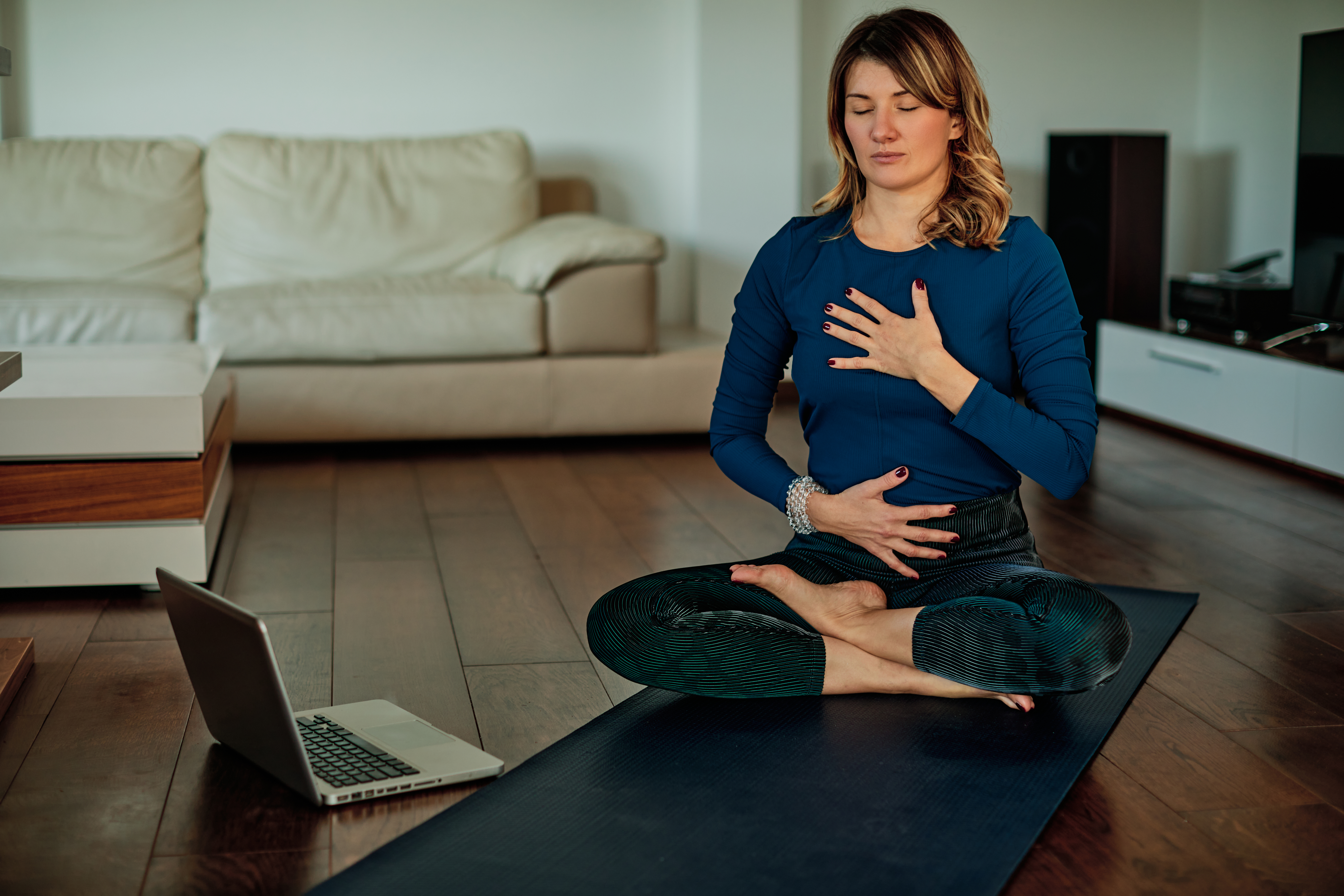 Middle-aged brunette sitting in lotus poses and meditating at home while following video tutorials.