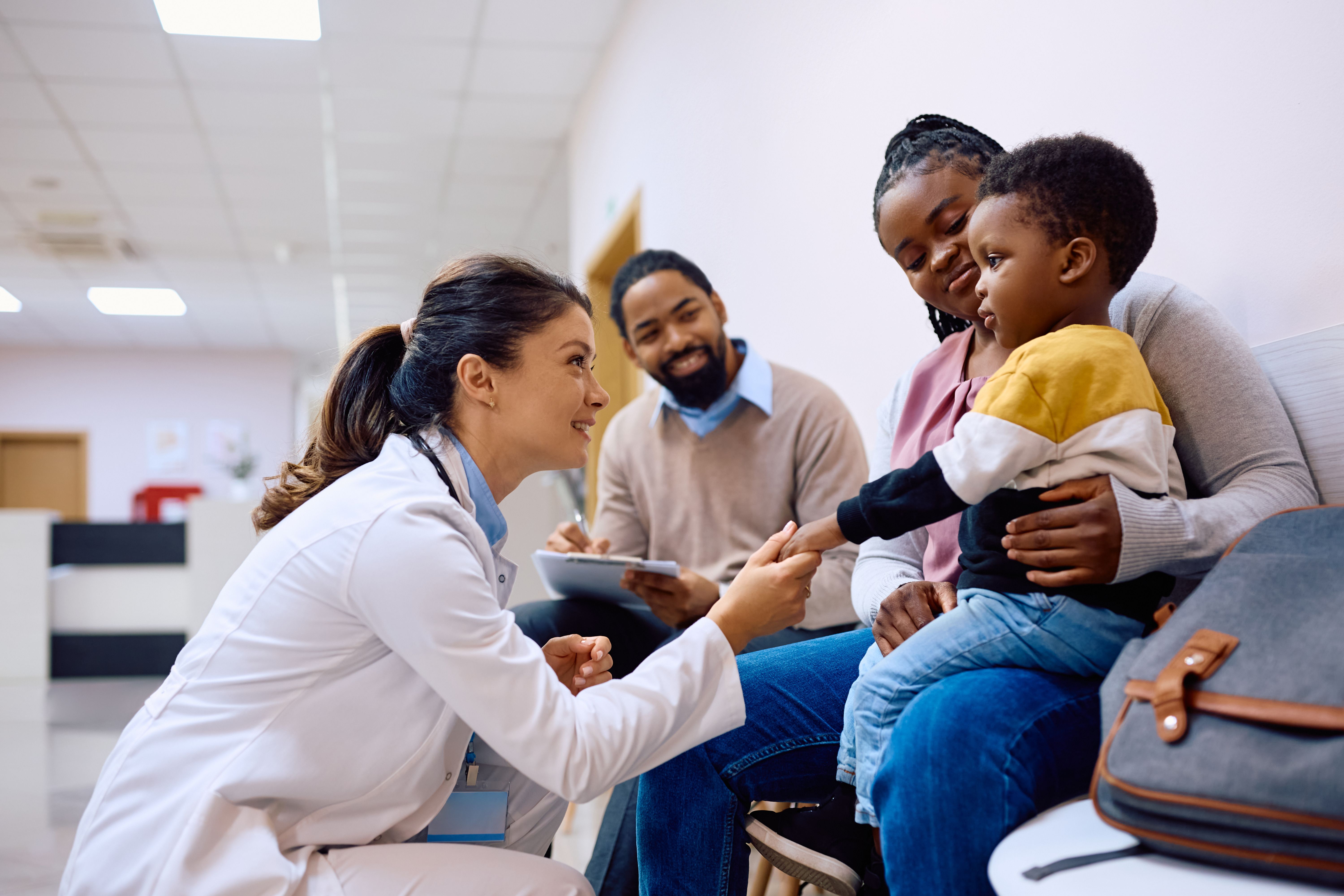 Female pediatrician talking to black little boy who is sitting on mother's lap at the clinic. Female pediatrician talking to black little boy who is sitting on mother's lap at the clinic.