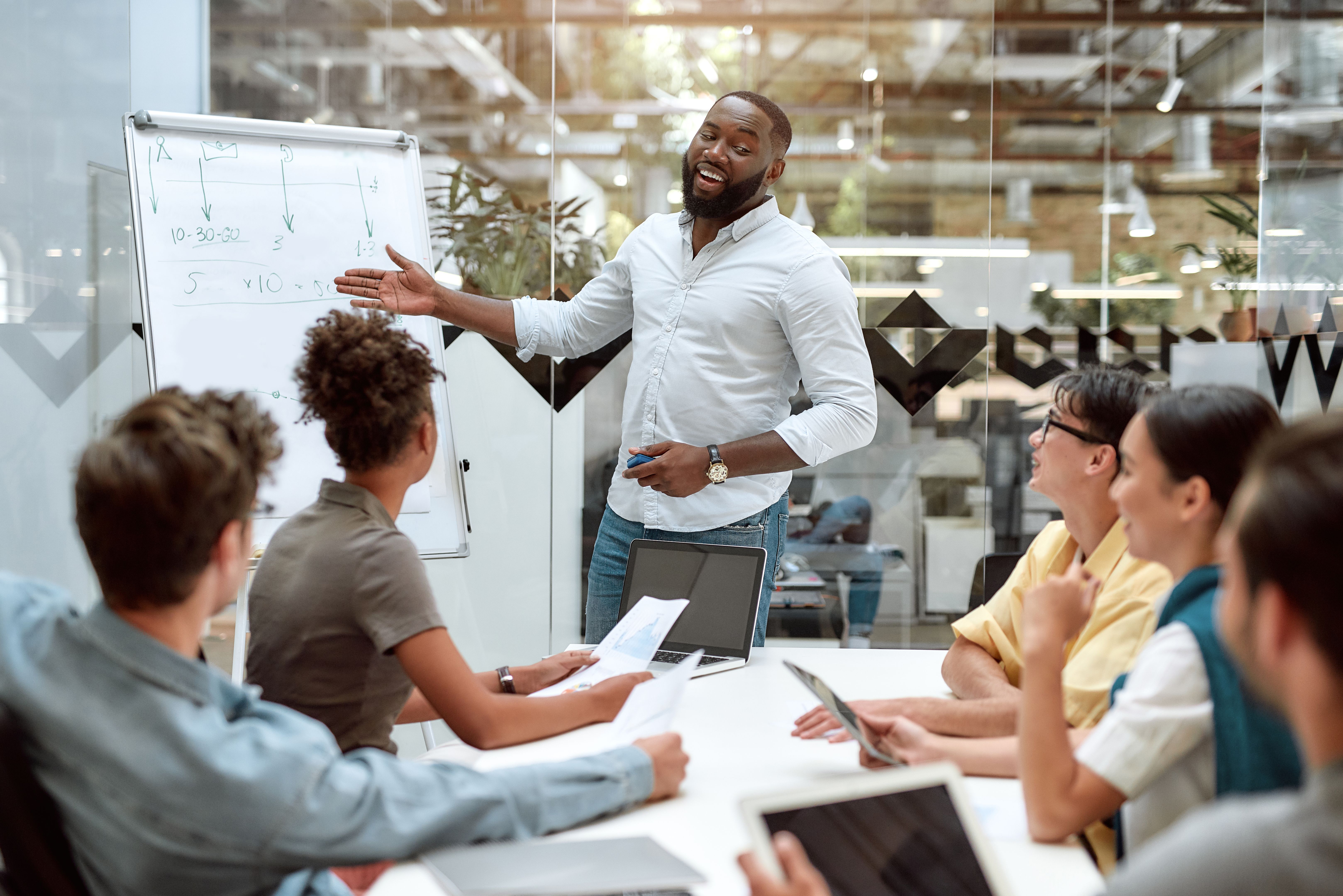 Achieving best results together. Young afro american businessman pointing at white blackboard and smiling while working with multicultural team in the creative office