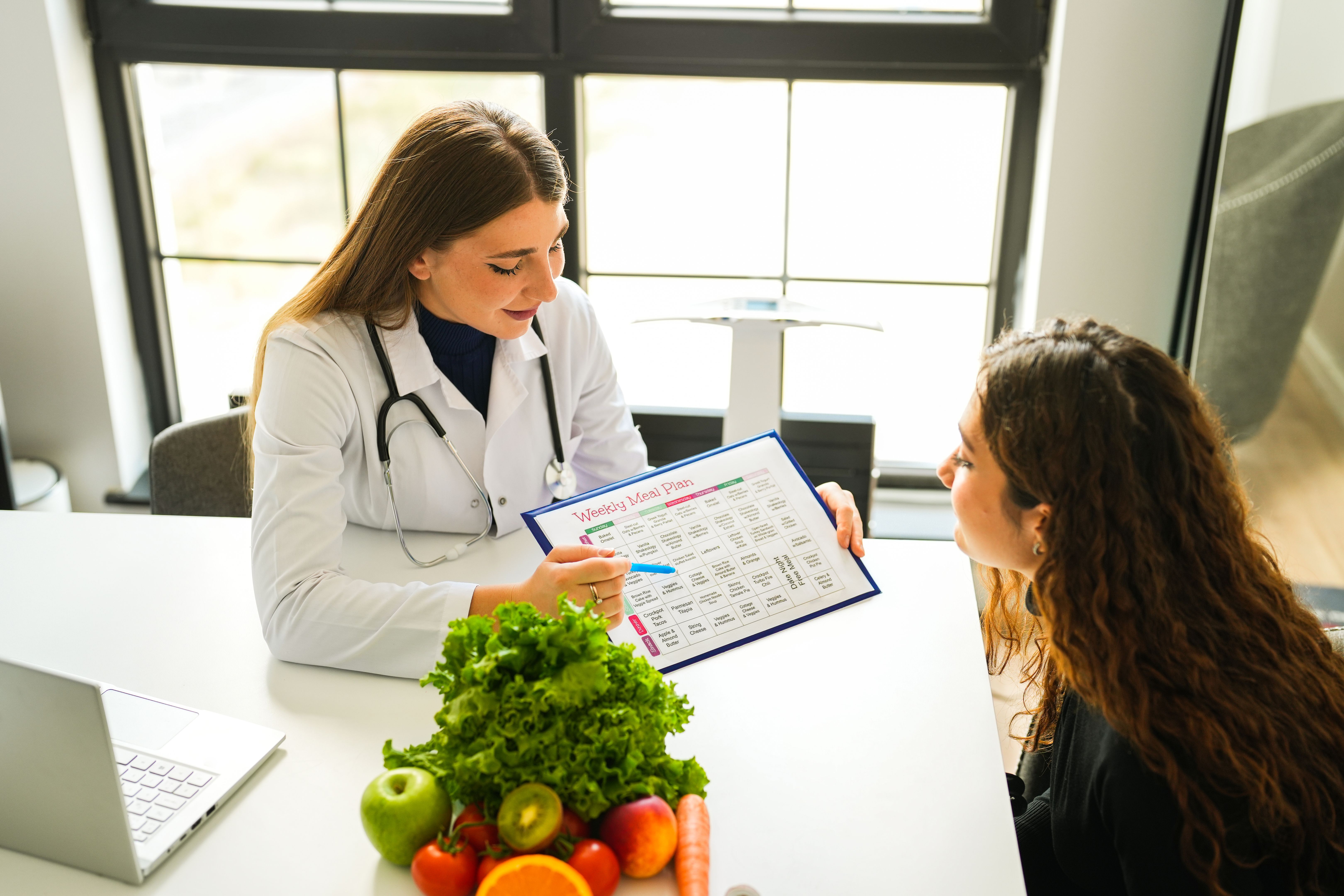 Beautiful blonde female healthy nutritionist showing her diet list to her client Beautiful blonde female healthy nutritionist showing her diet list to her client