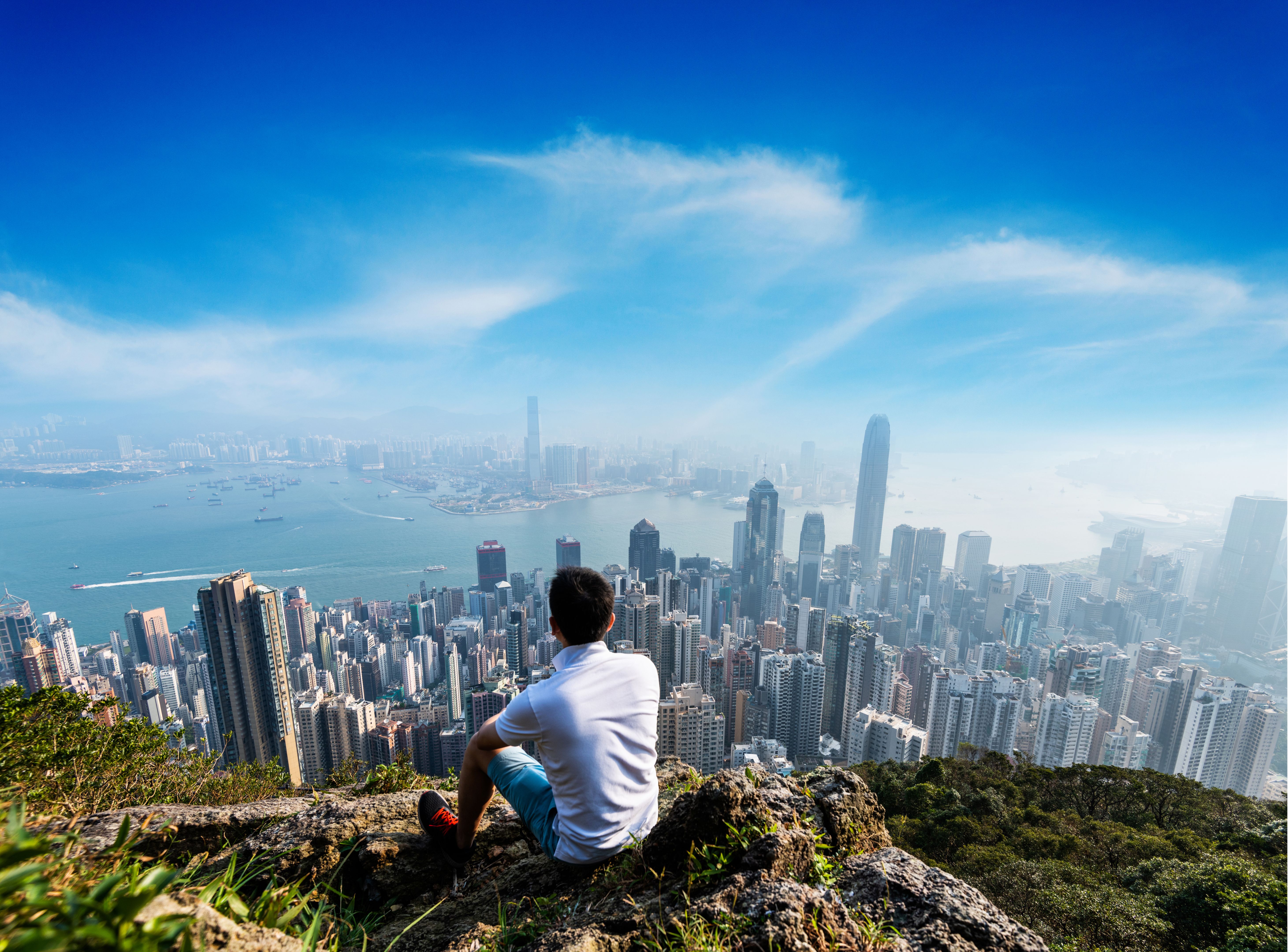 Young man sitting on top of mountain and looking at hong kong skyline
