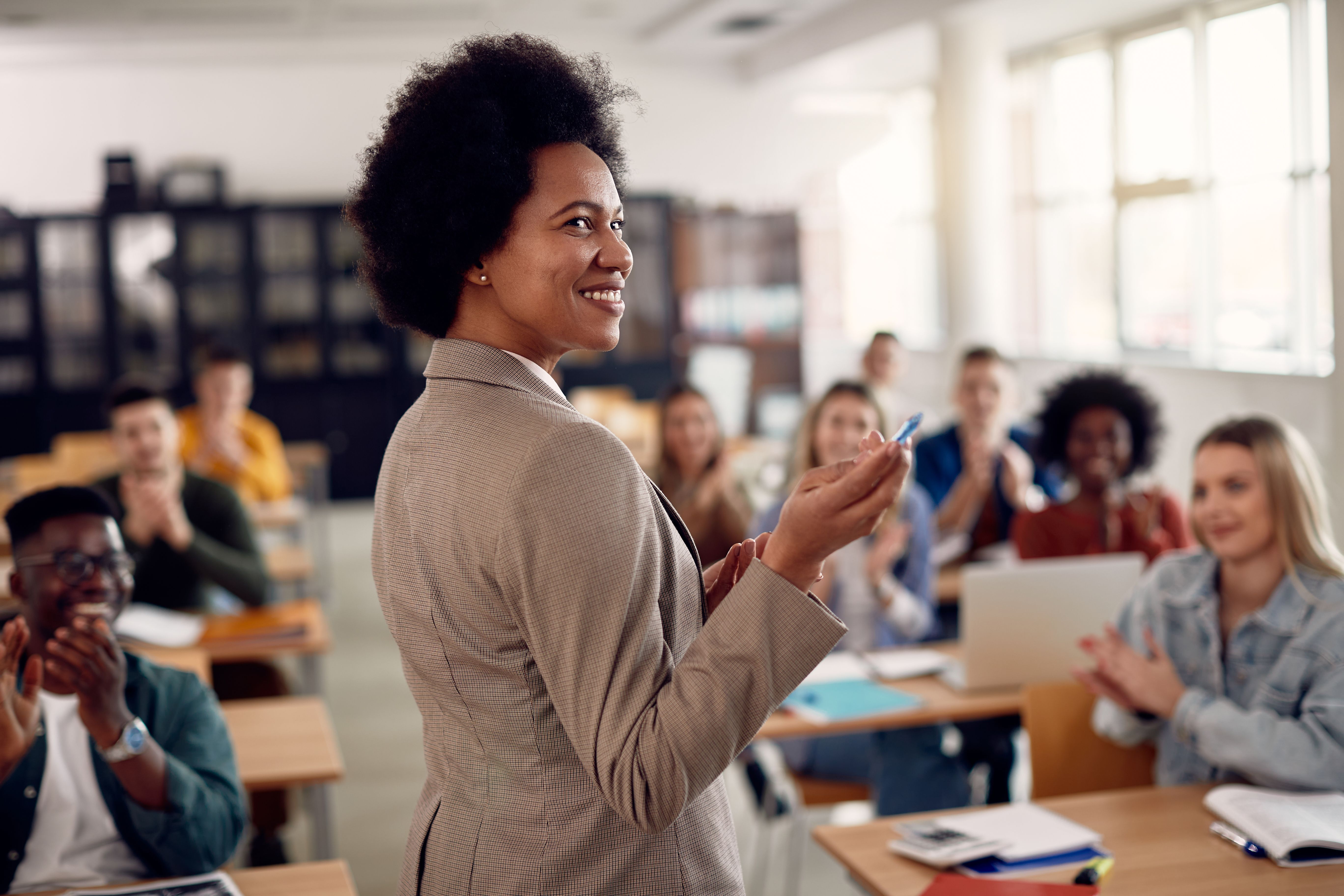 Happy black techer getting applause from her students after giving them a lecture at the university.