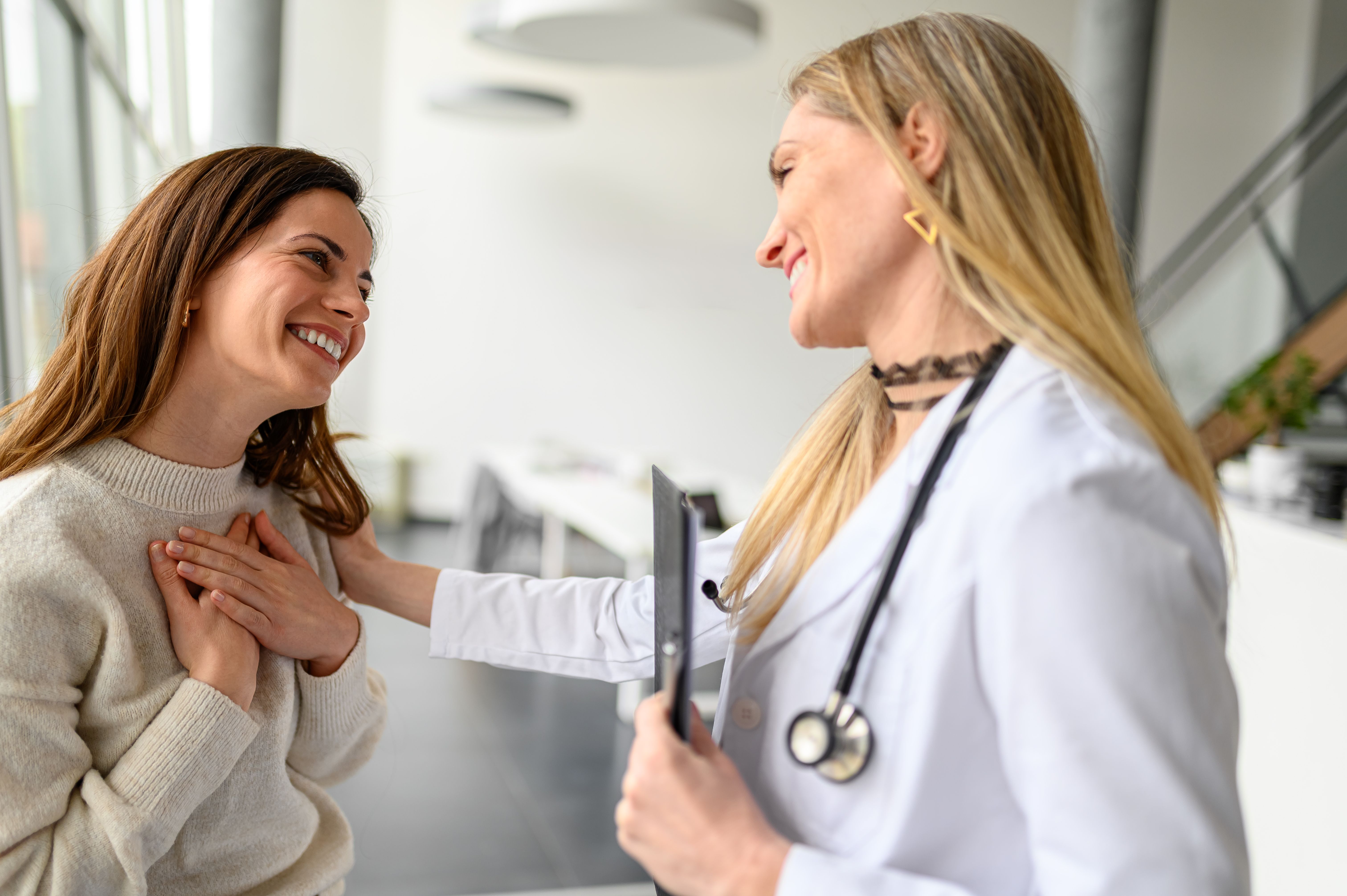 Smiling woman expressing her gratitude to female doctor in hospital during medical consultation Smiling woman expressing her gratitude to female doctor in hospital during medical consultation