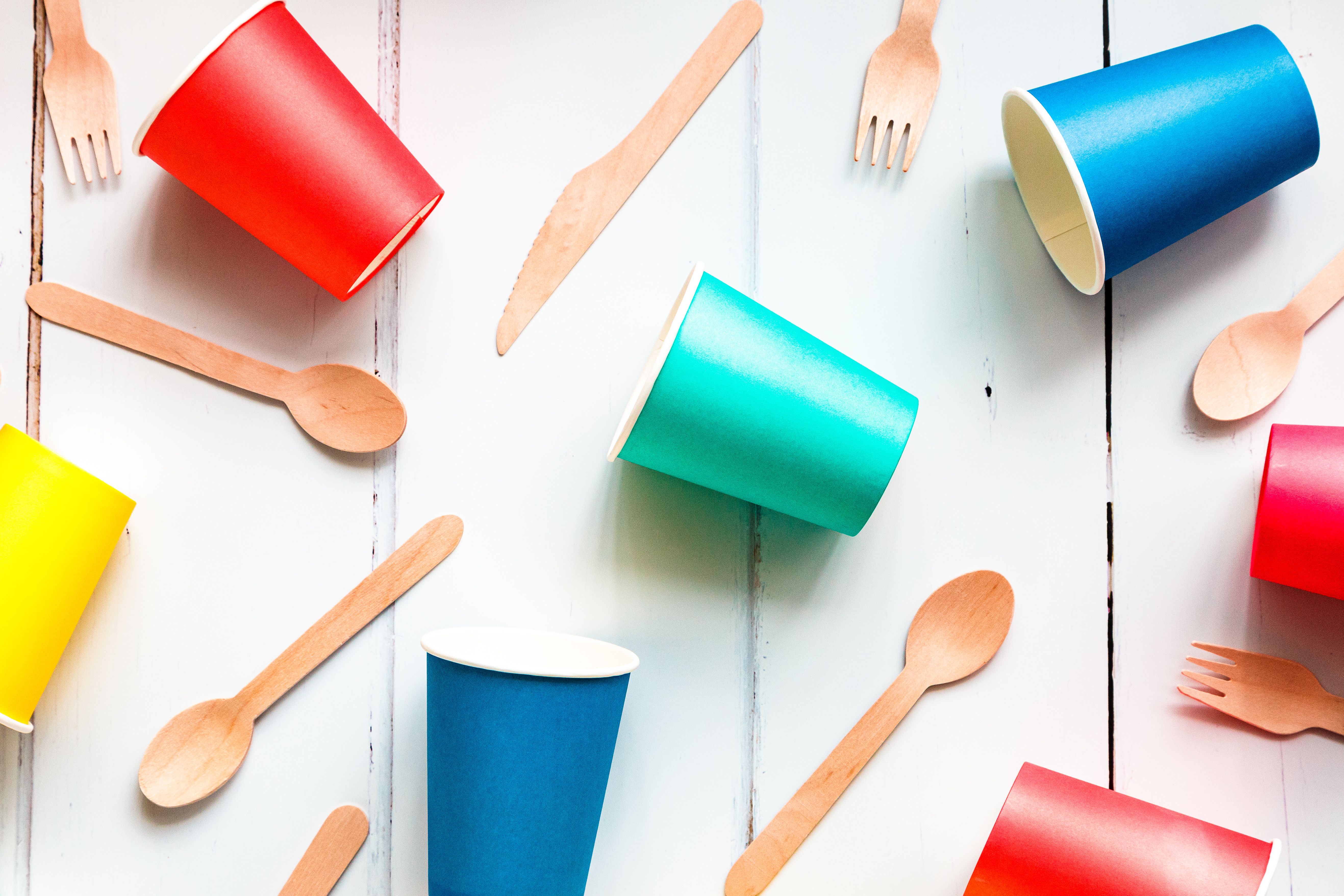 Colorful recyclable paper cups and wooden kitchenware utensils on white background